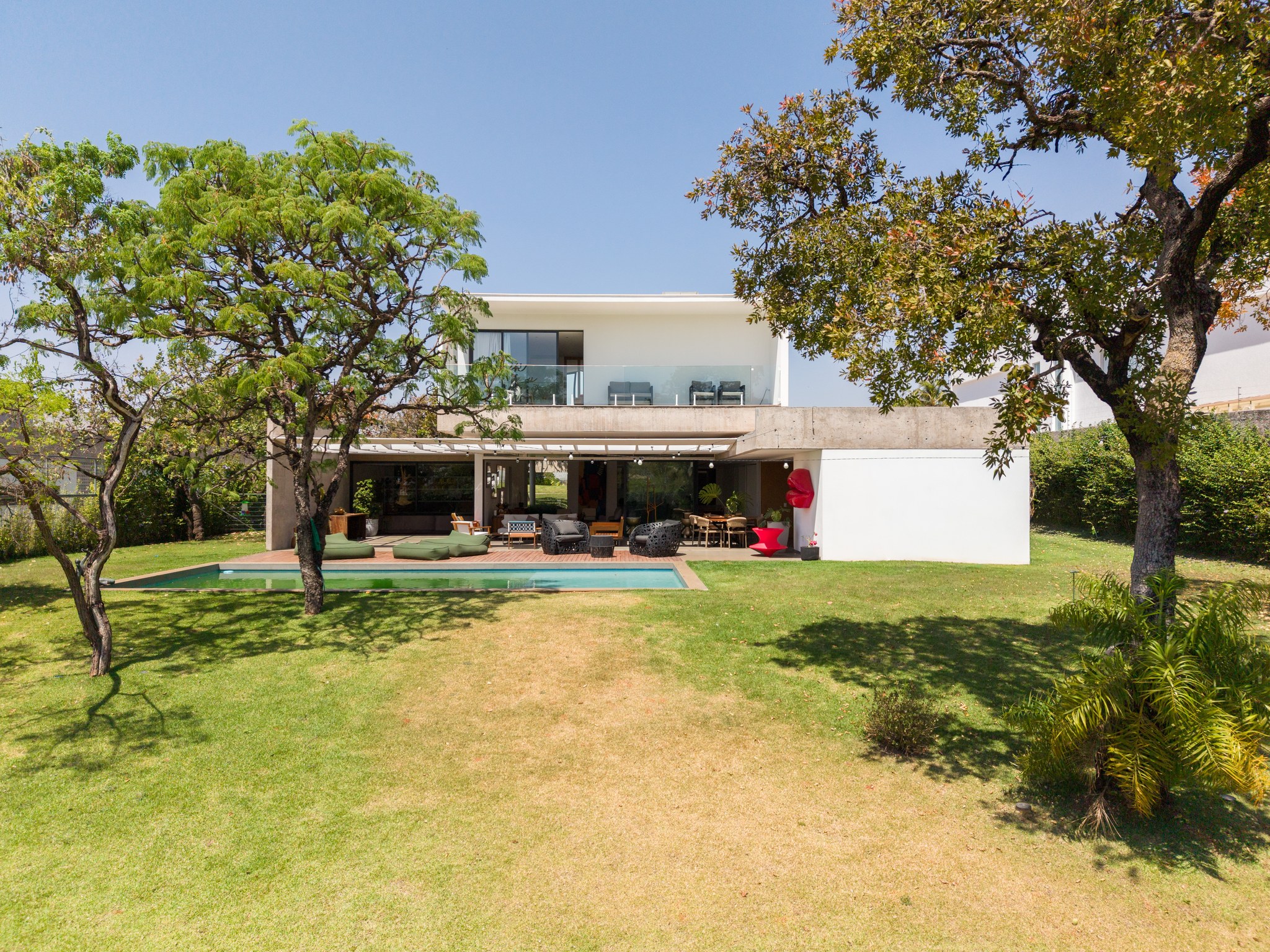 Fachada dos fundos da casa vista do jardim, com pérgola sobre a piscina e área de estar coberta