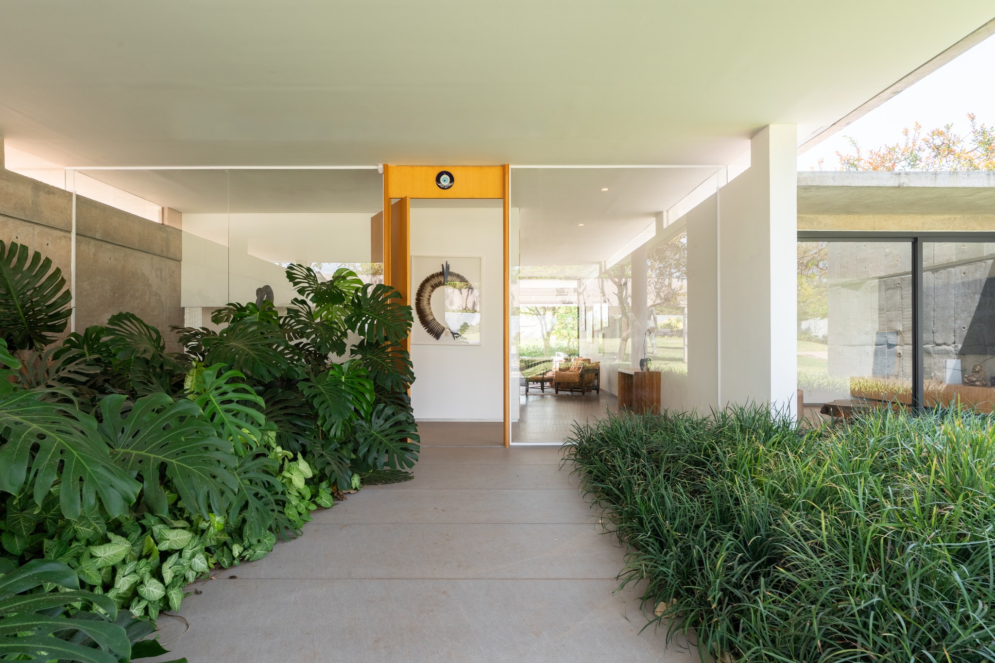 Hall de entrada com porta em madeira e amarelo, escultura em resina e obra emoldurada ao fundo