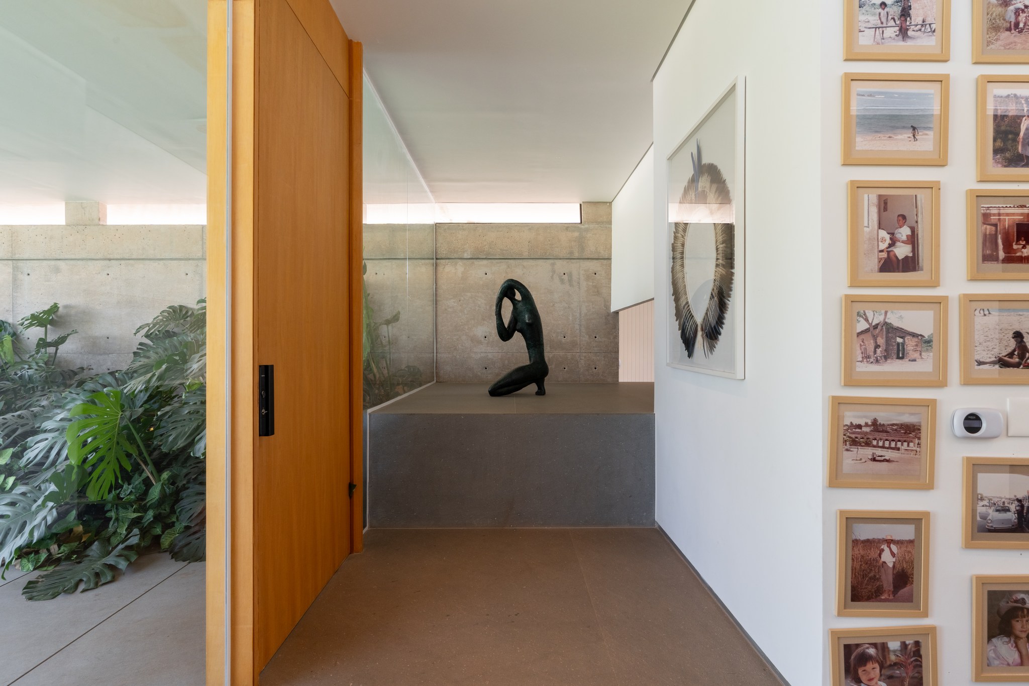 Hall interno com escultura em bronze sobre base de concreto, ao lado de um mural de fotografias de família