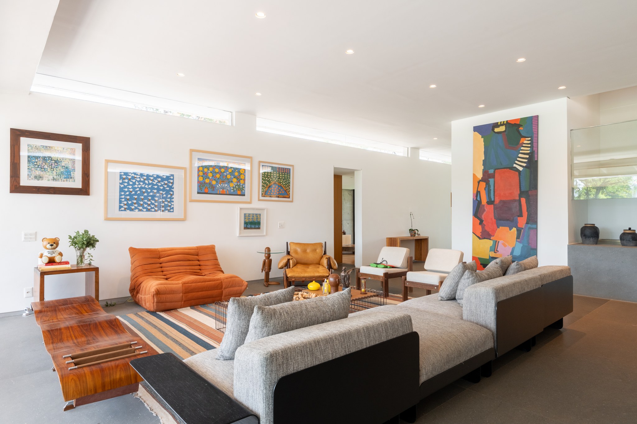 Sala de estar com galeria de quadros coloridos, sofá Togo laranja e pintura abstrata vertical ao fundo
