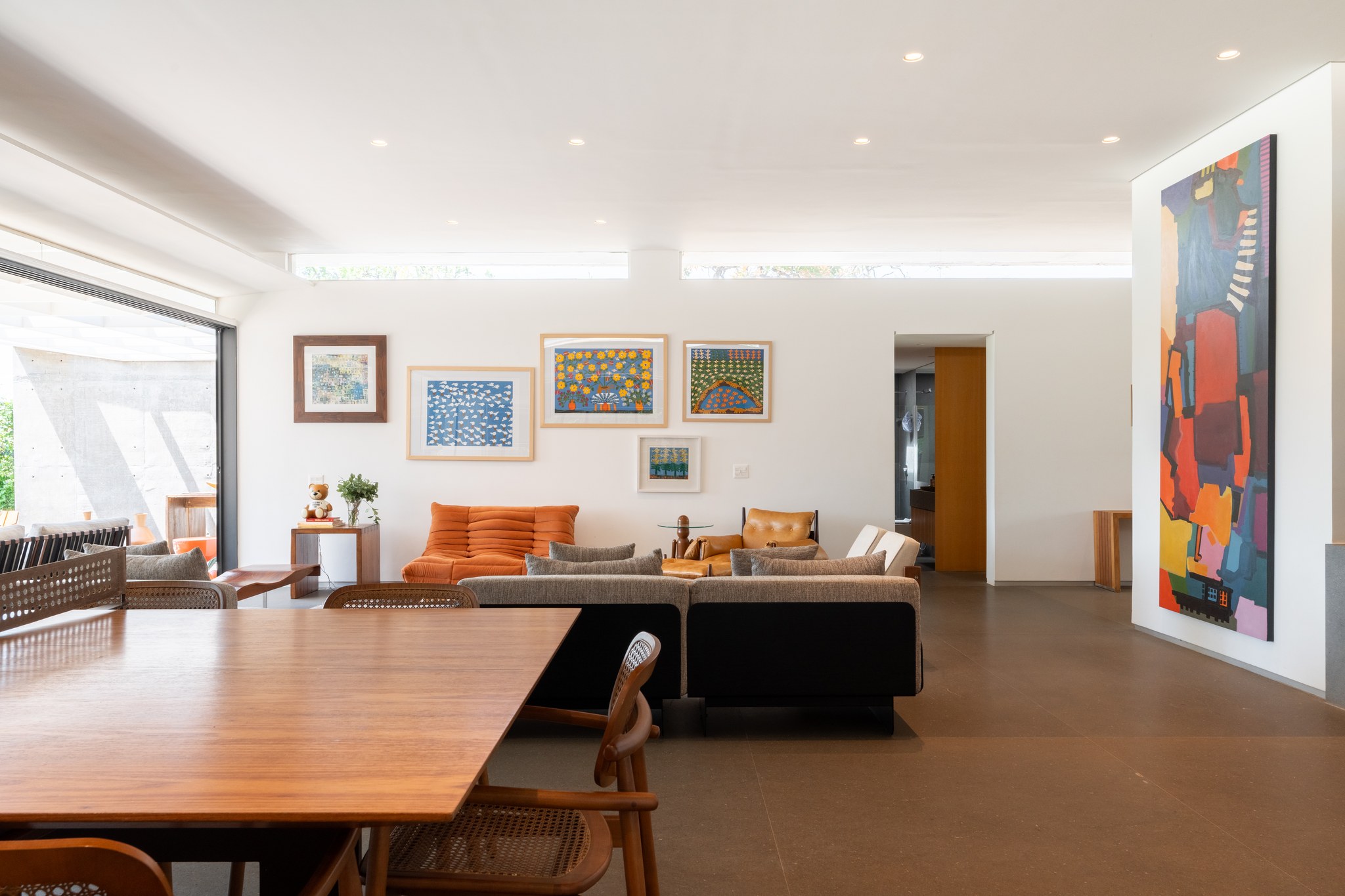 Sala de estar com galeria de arte naïf, sofá modular cinza e pintura abstrata vertical junto à escada