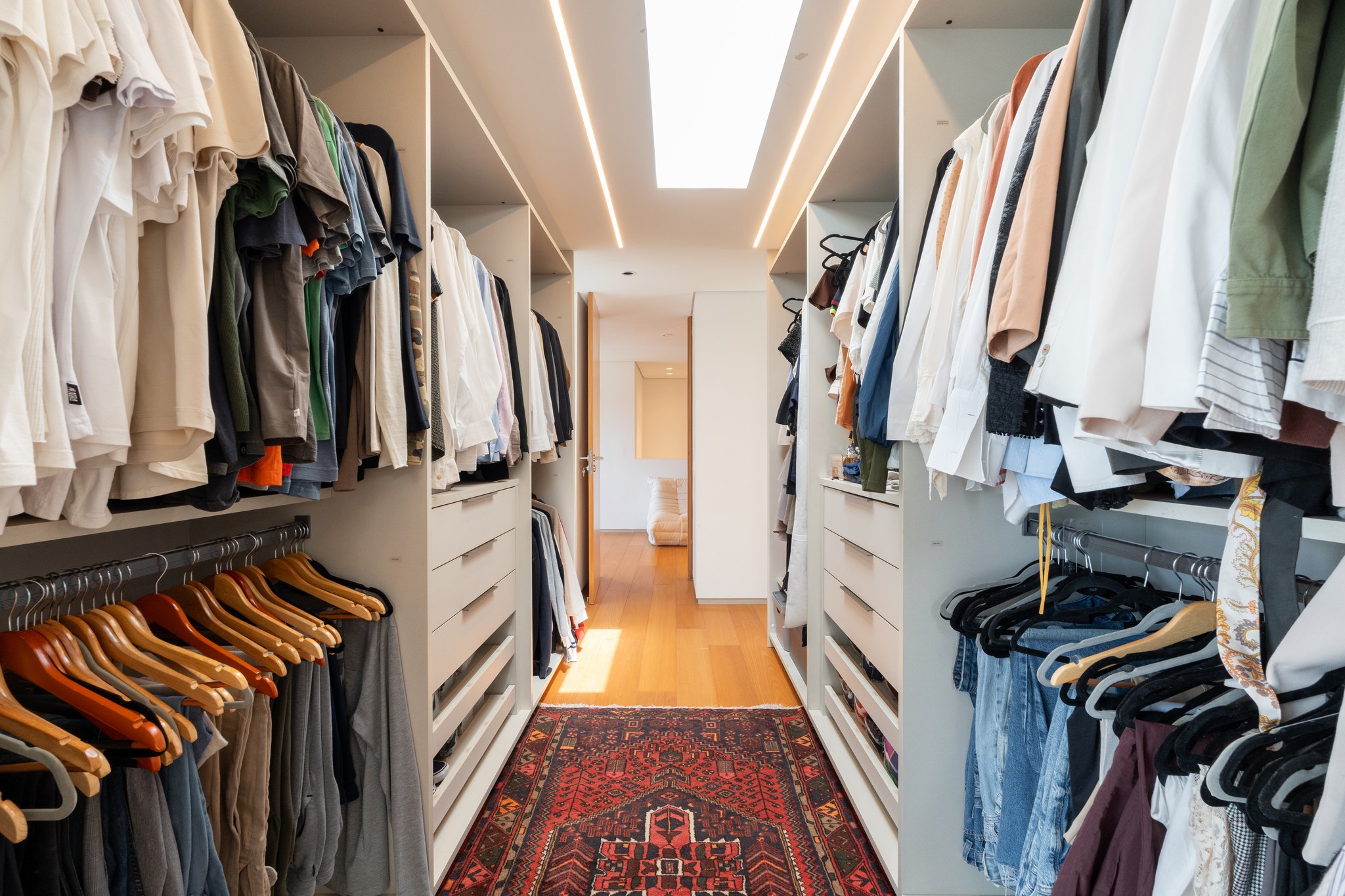 Closet com araras de roupas dos dois lados, tapete persa vermelho e claraboia central
