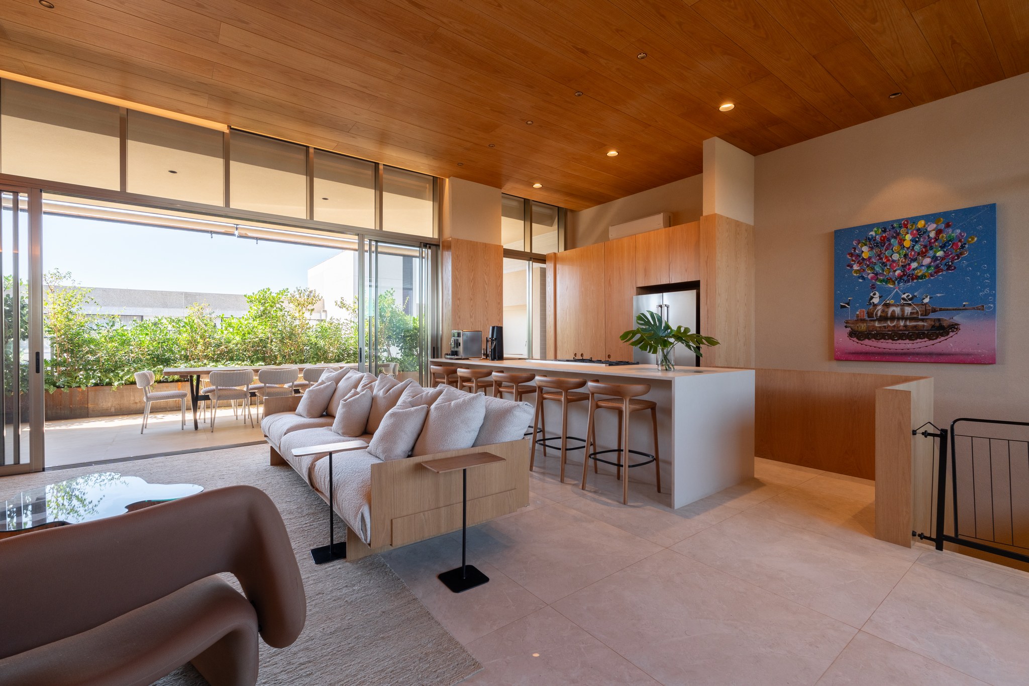 Sala de estar integrada à cozinha em madeira, com sofá bege e quadro colorido de tanque