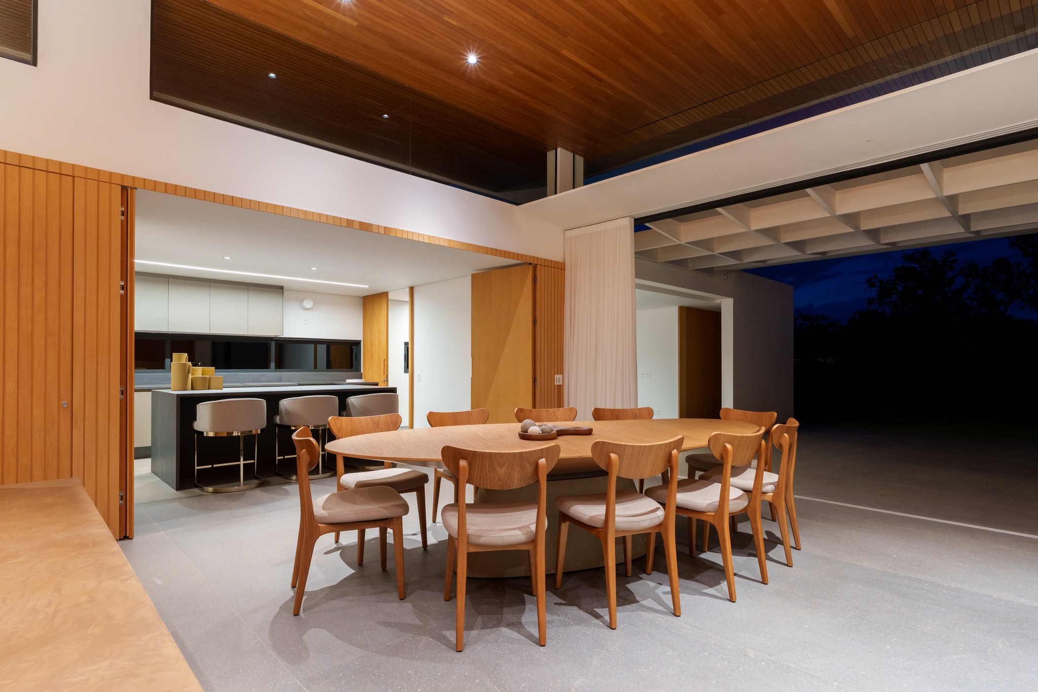 Sala de jantar ampla com iluminação noturna e cozinha ao fundo