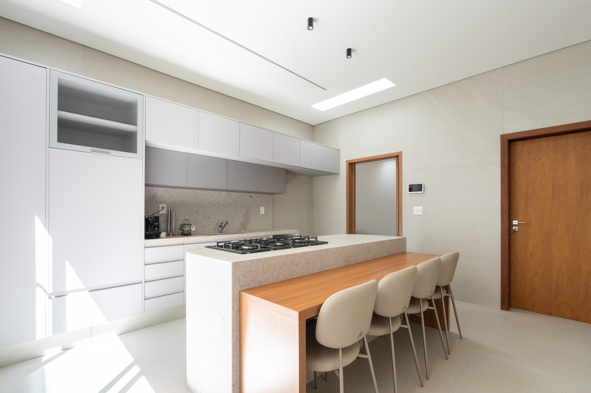 Cozinha com ilha central em granito, cooktop a gás e porta de vidro jateado para o corredor