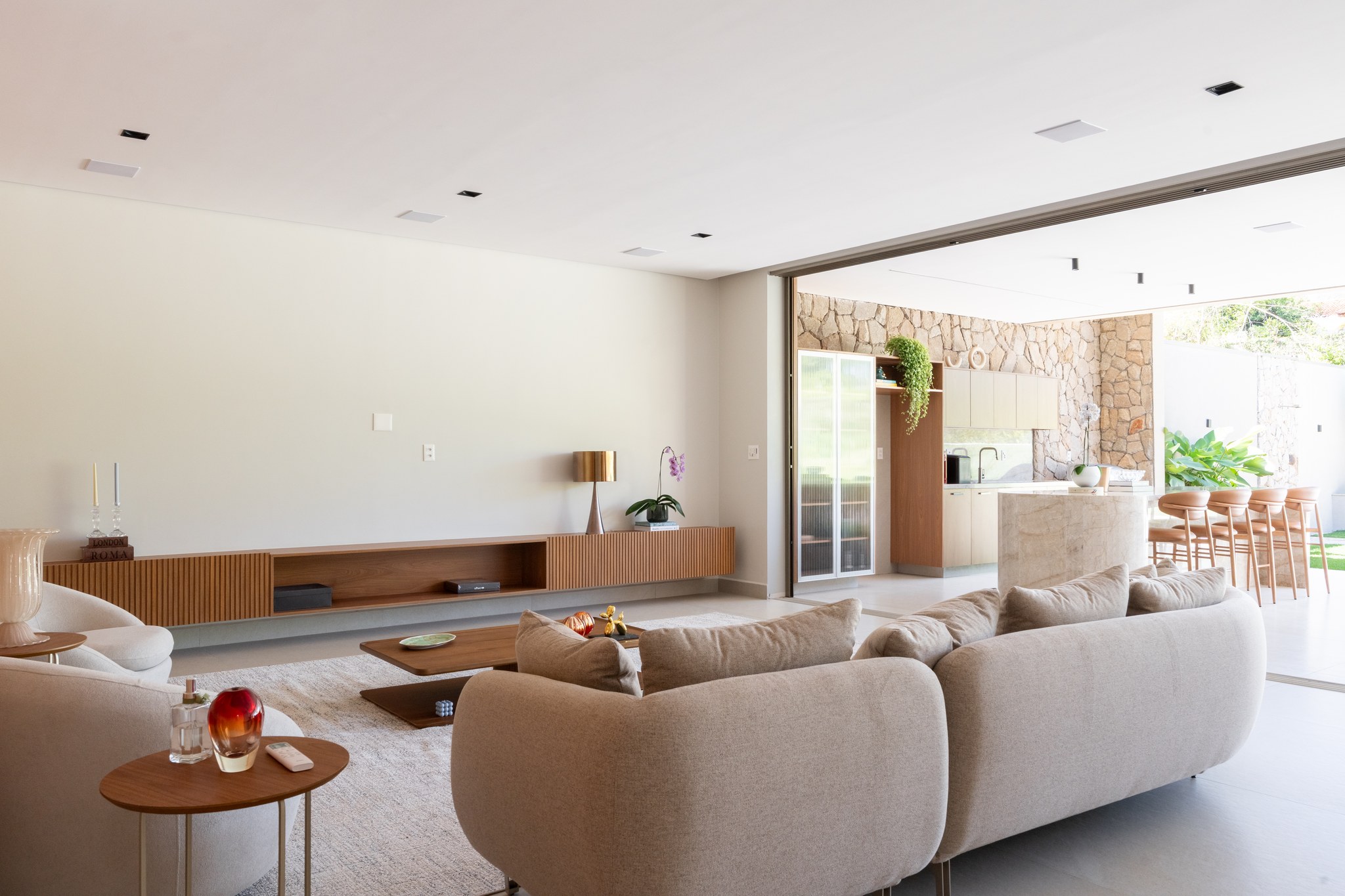 Sala de estar com sofá bege modular, poltronas terracota e porta pivotante em madeira ao fundo