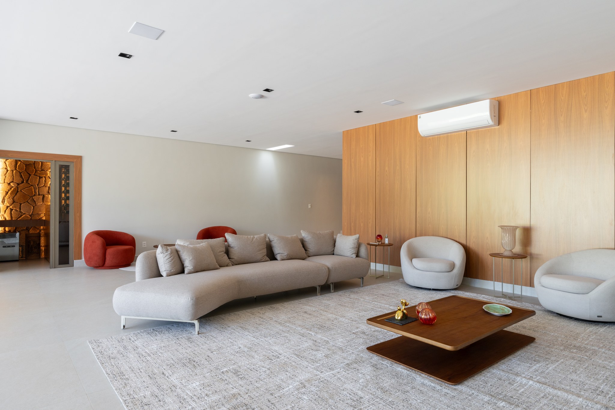 Sala de estar com sofá cinza claro, poltronas terracota e painel de madeira com ar-condicionado split