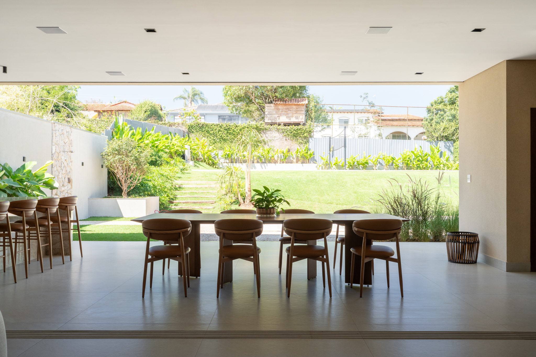 Área externa coberta com mesa de jantar para dez lugares e jardim amplo ao fundo