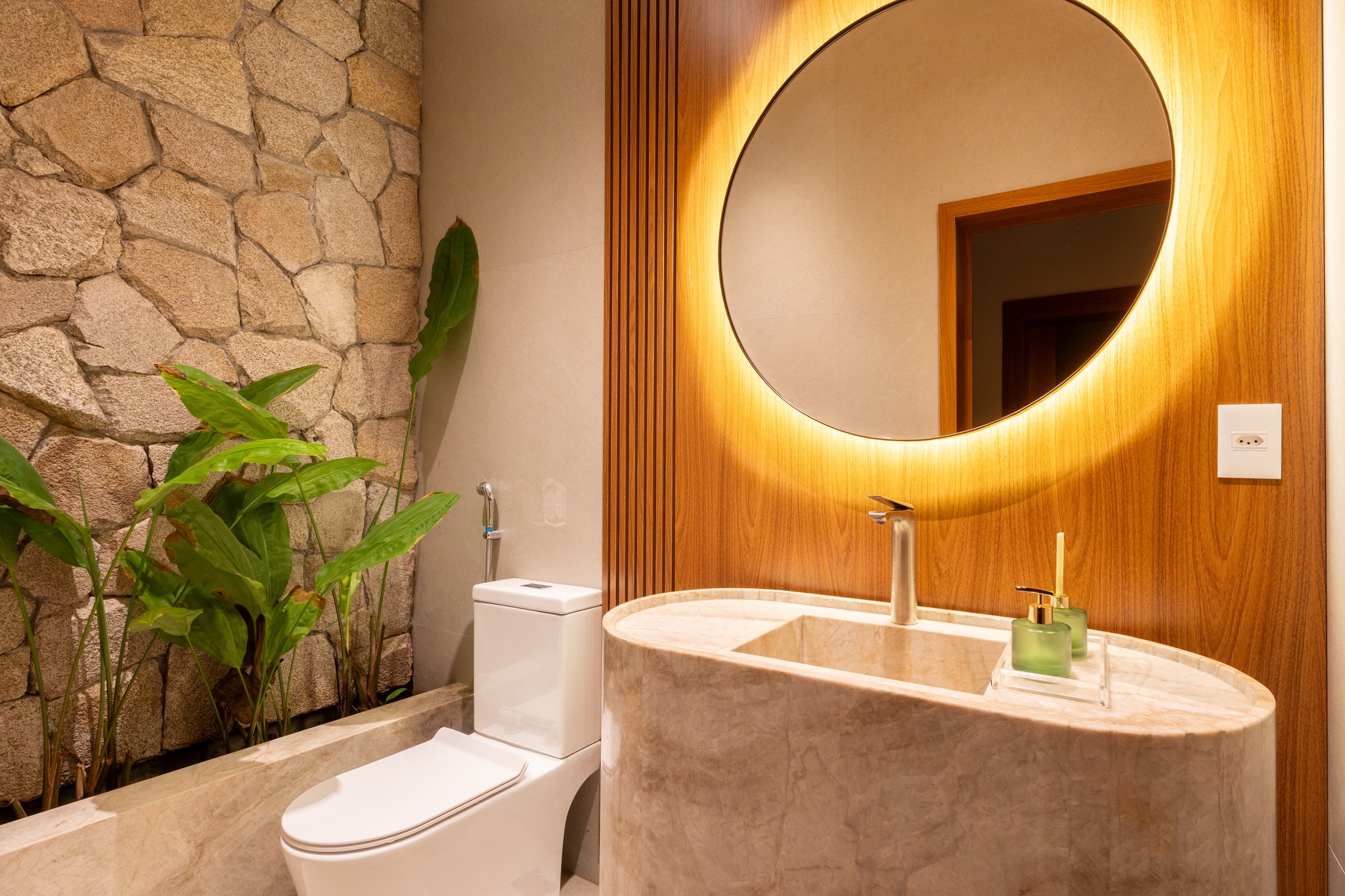 Lavabo à noite, com espelho redondo retroiluminado e pia esculpida em mármore
