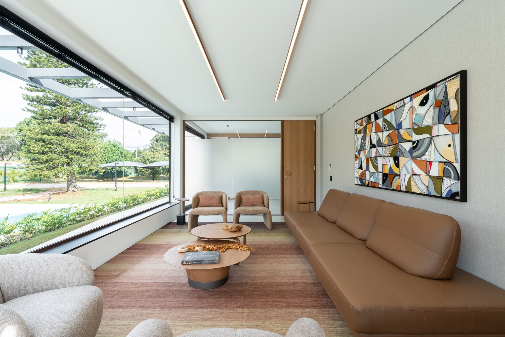 Sala de estar com quadro de colagem colorida, sofás em couro caramelo e vista para pérgola externa