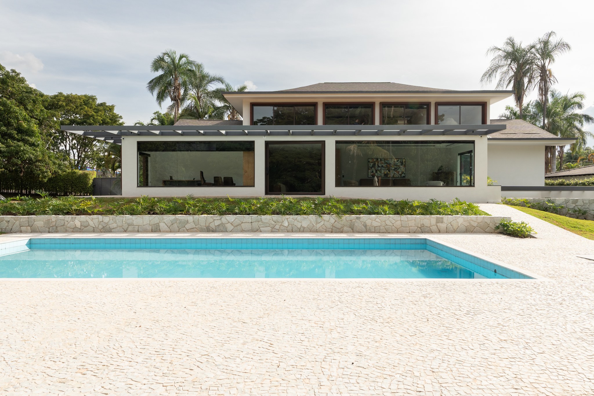 Fachada dos fundos com piscina, pérgola metálica e ampla esquadria de vidro integrando os ambientes