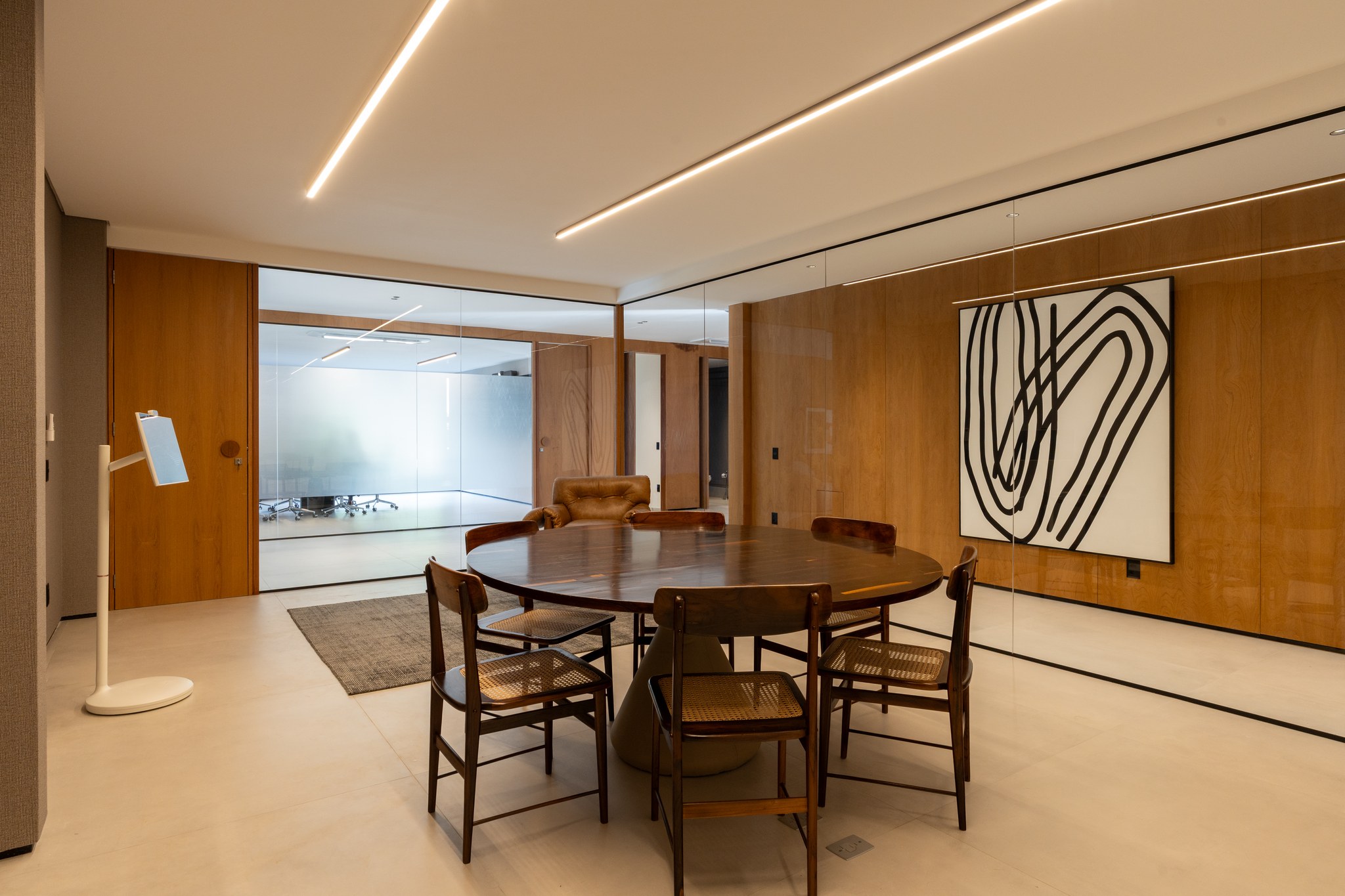Sala de jantar com mesa redonda de madeira maciça, cadeiras em palhinha e pintura abstrata em preto e branco