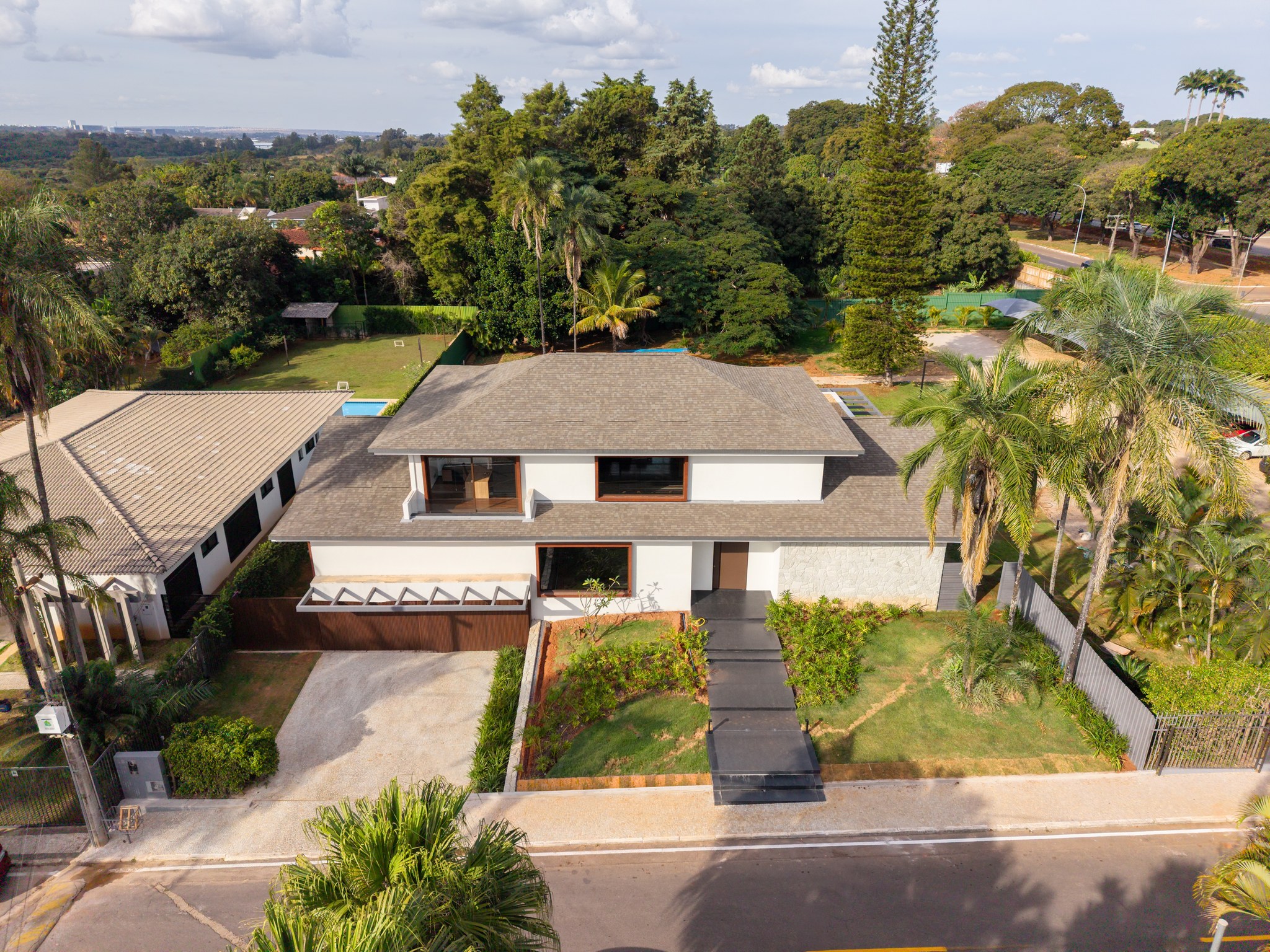 Vista aérea da fachada frontal da casa, cercada por palmeiras e vegetação densa do entorno