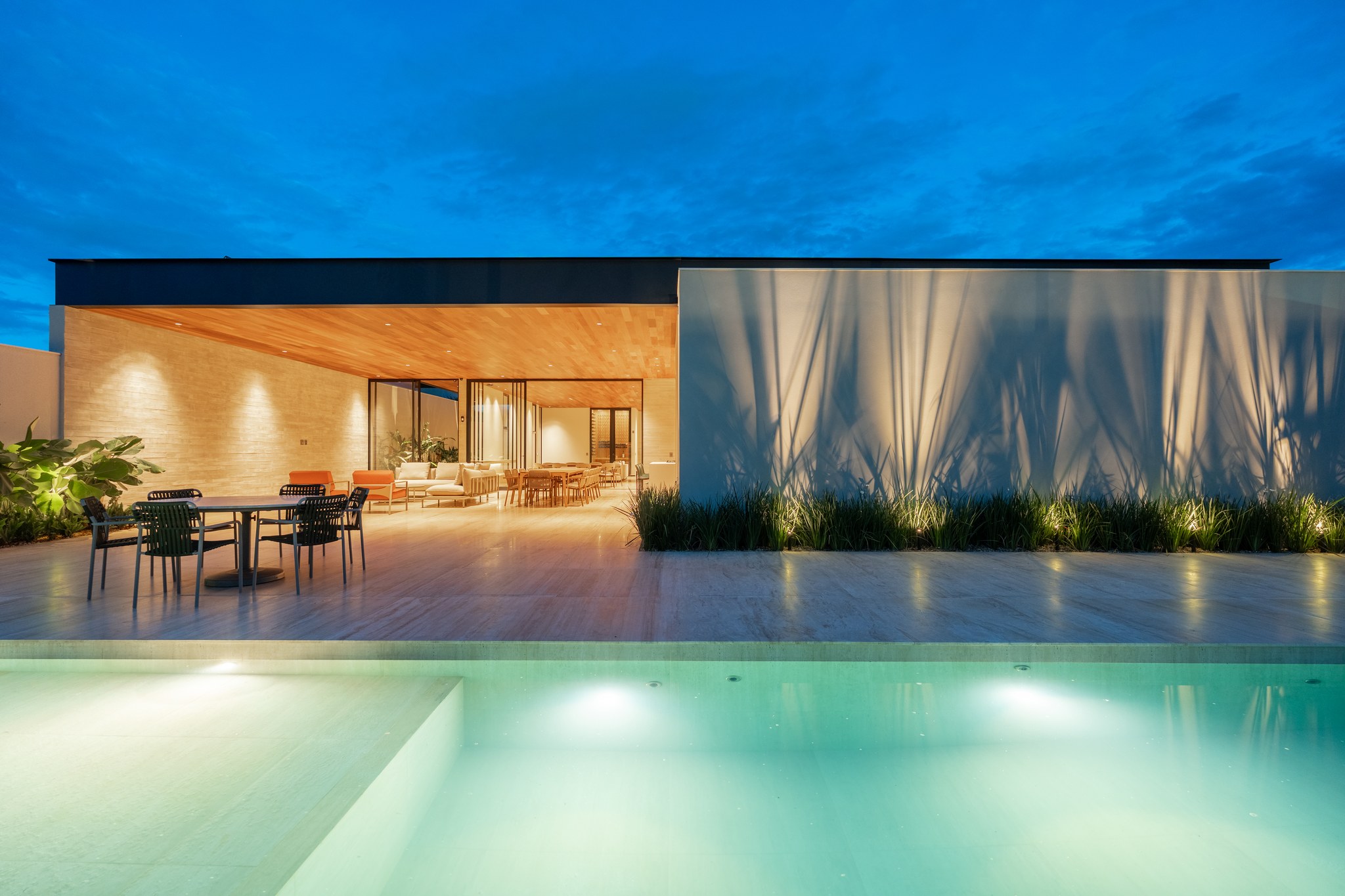 Fachada dos fundos ao entardecer, com piscina iluminada e área de estar integrada