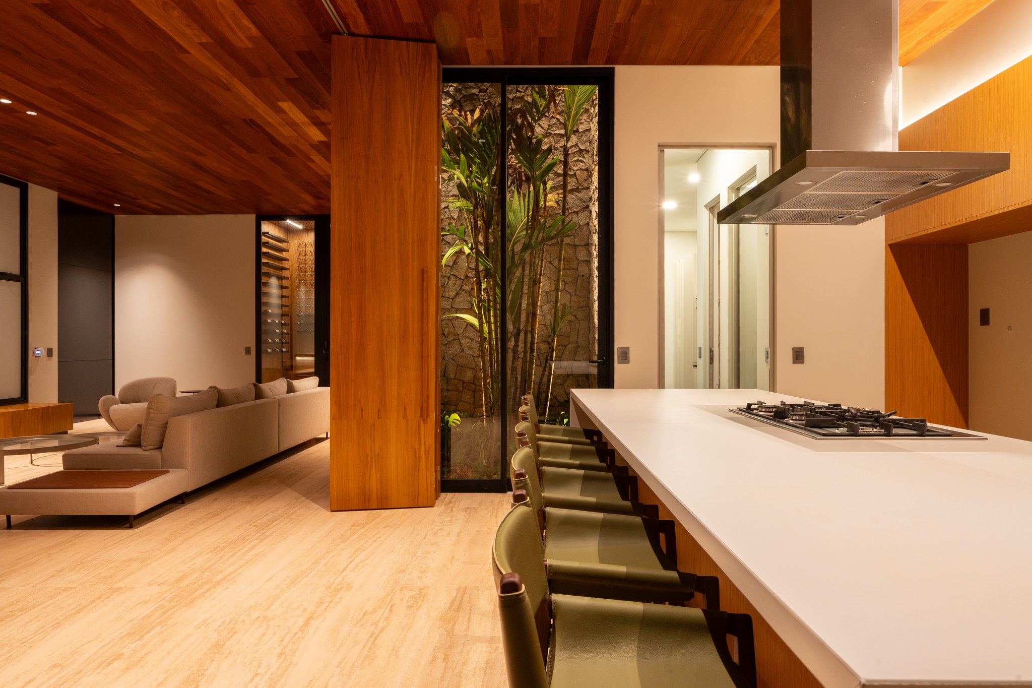 Sala de estar integrada à cozinha, com jardim de inverno em pedra entre os ambientes