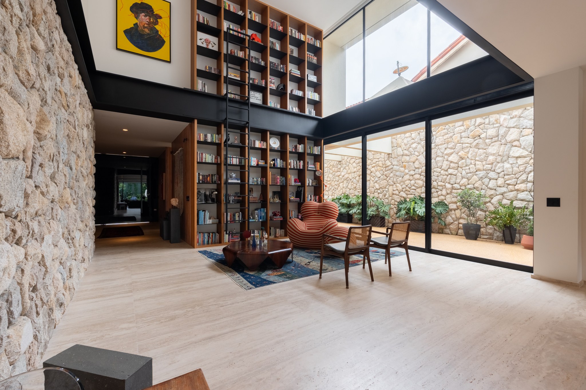 Sala de estar com pé-direito duplo, estante de livros com escada e claraboia lateral