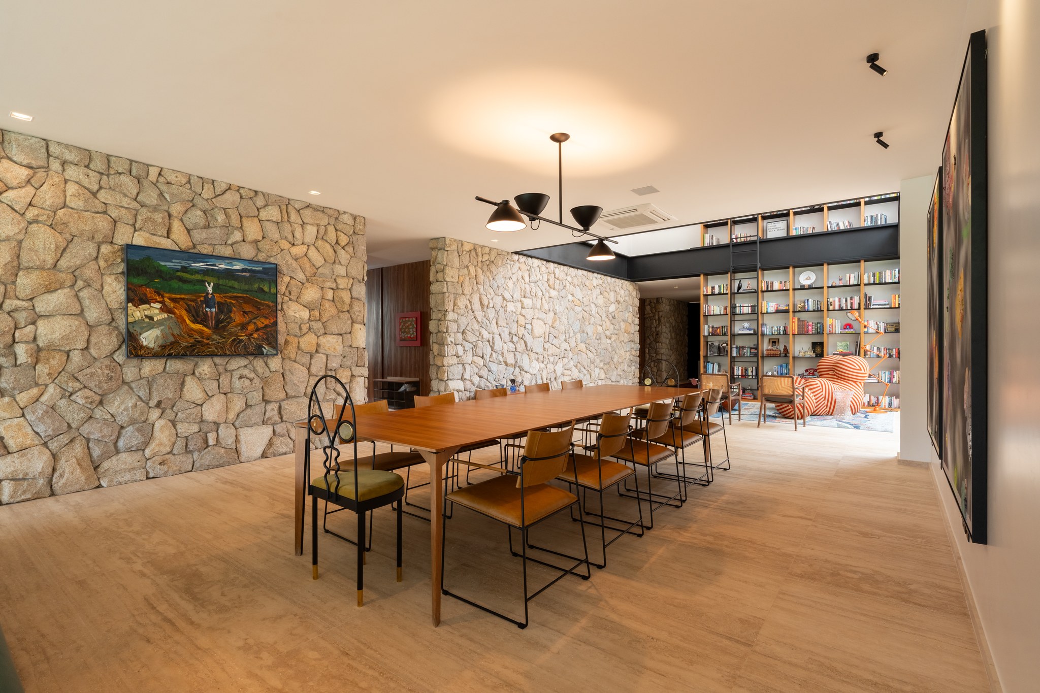 Sala de jantar com mesa para doze lugares, parede em pedra e biblioteca ao fundo