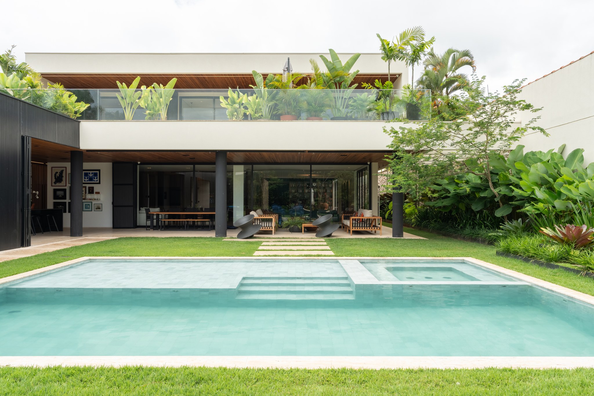 Fachada dos fundos em dois pavimentos, com piscina, jardim tropical e área de estar coberta