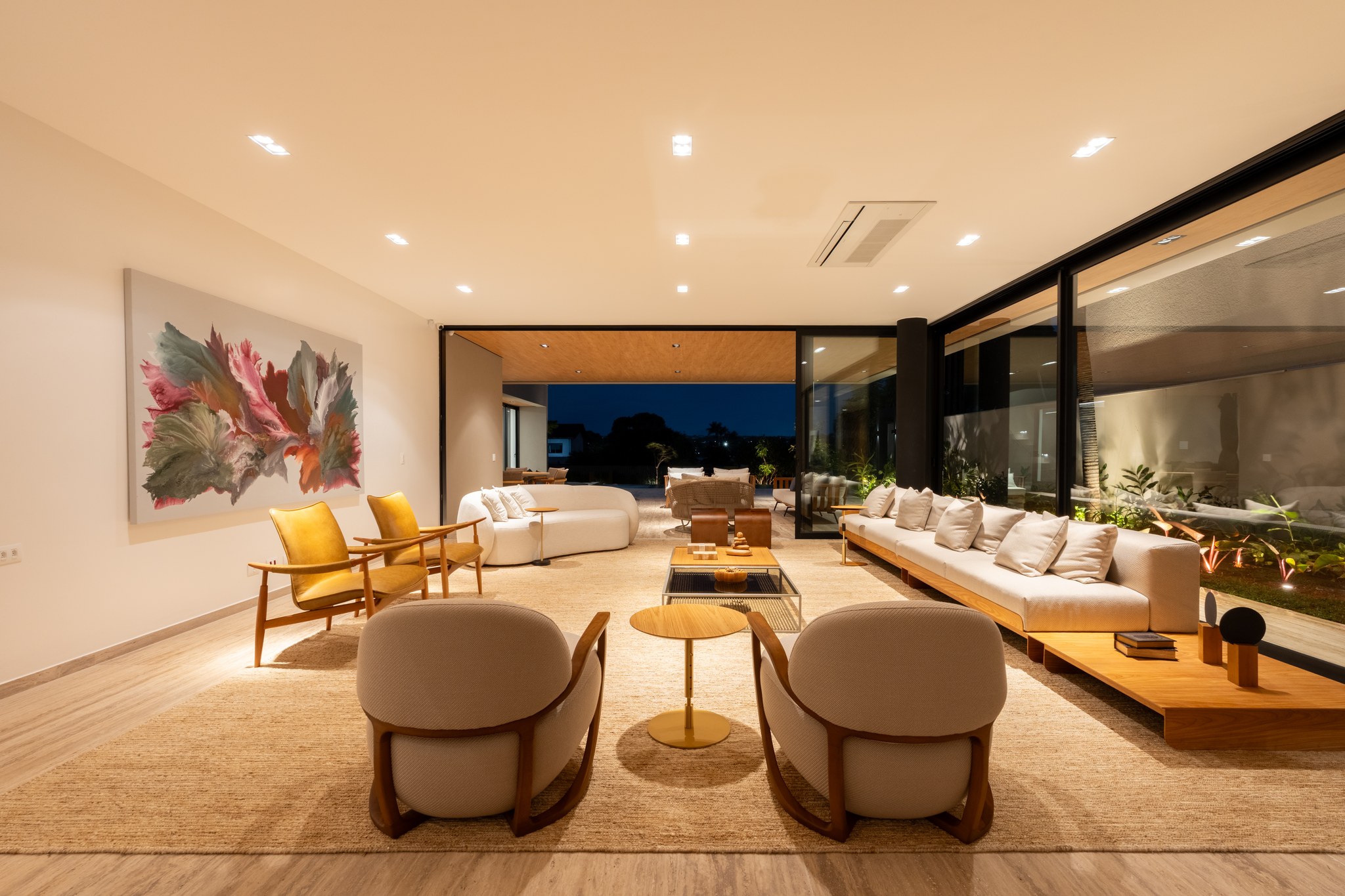 Sala de estar com poltronas amarelas, sofá branco modular e vista para a piscina à noite