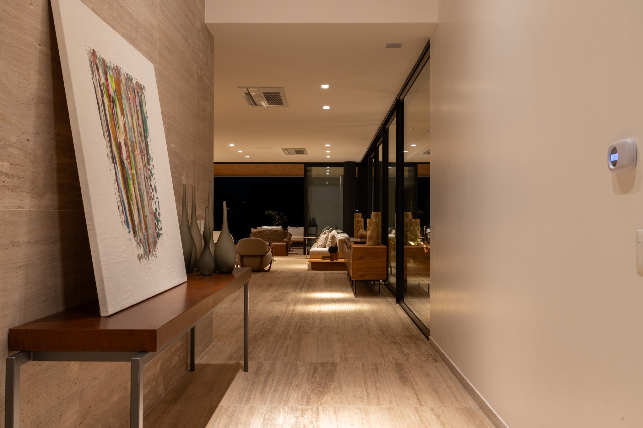 Sala de jantar com mesa de madeira, escultura em pedra e escada suspensa em travertino ao fundo