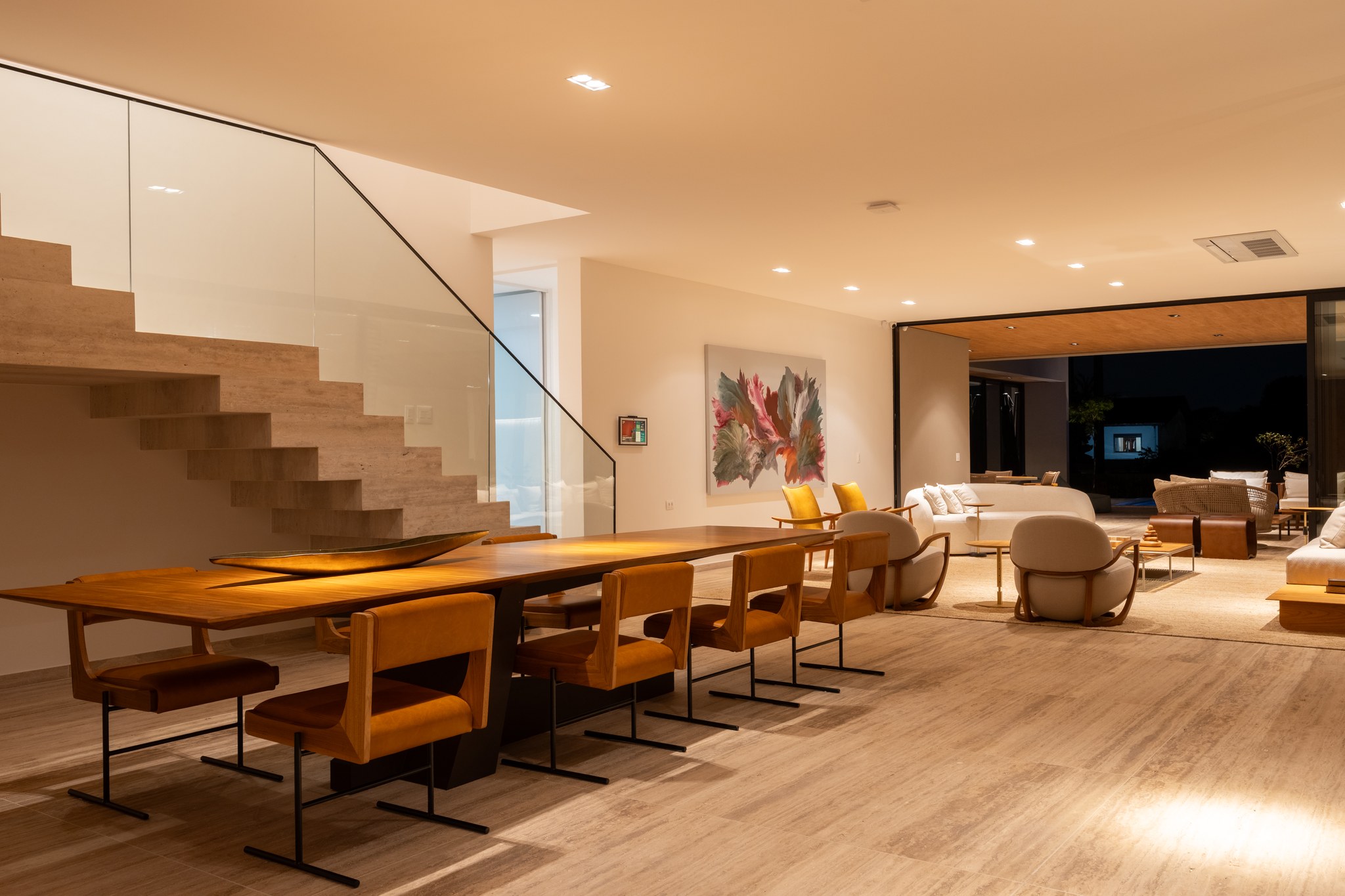 Sala de estar integrada à sala de jantar, com poltronas amarelas e vista noturna para a piscina