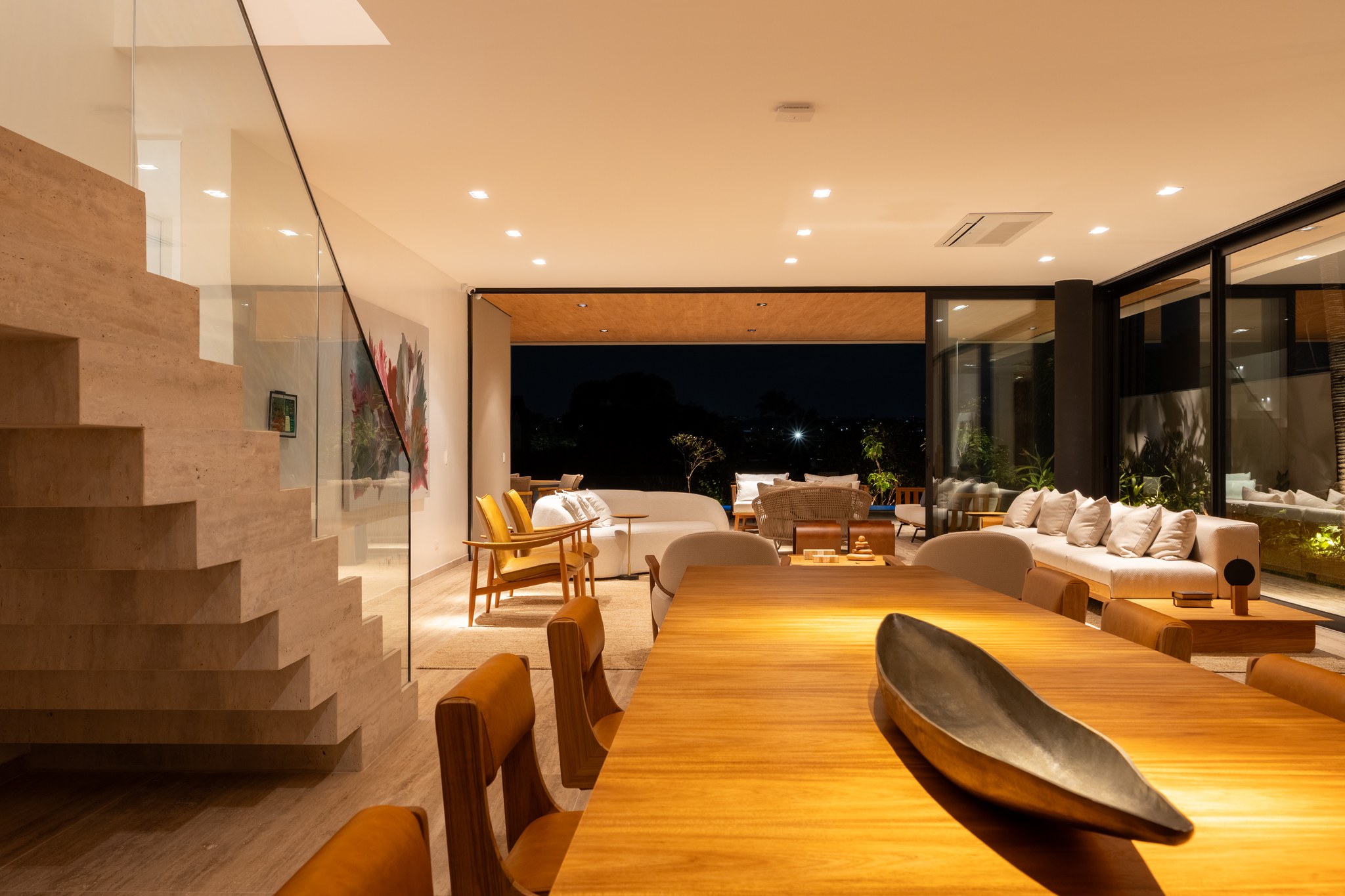 Sala de estar com escada em travertino, quadro colorido e sofás claros voltados para o jardim