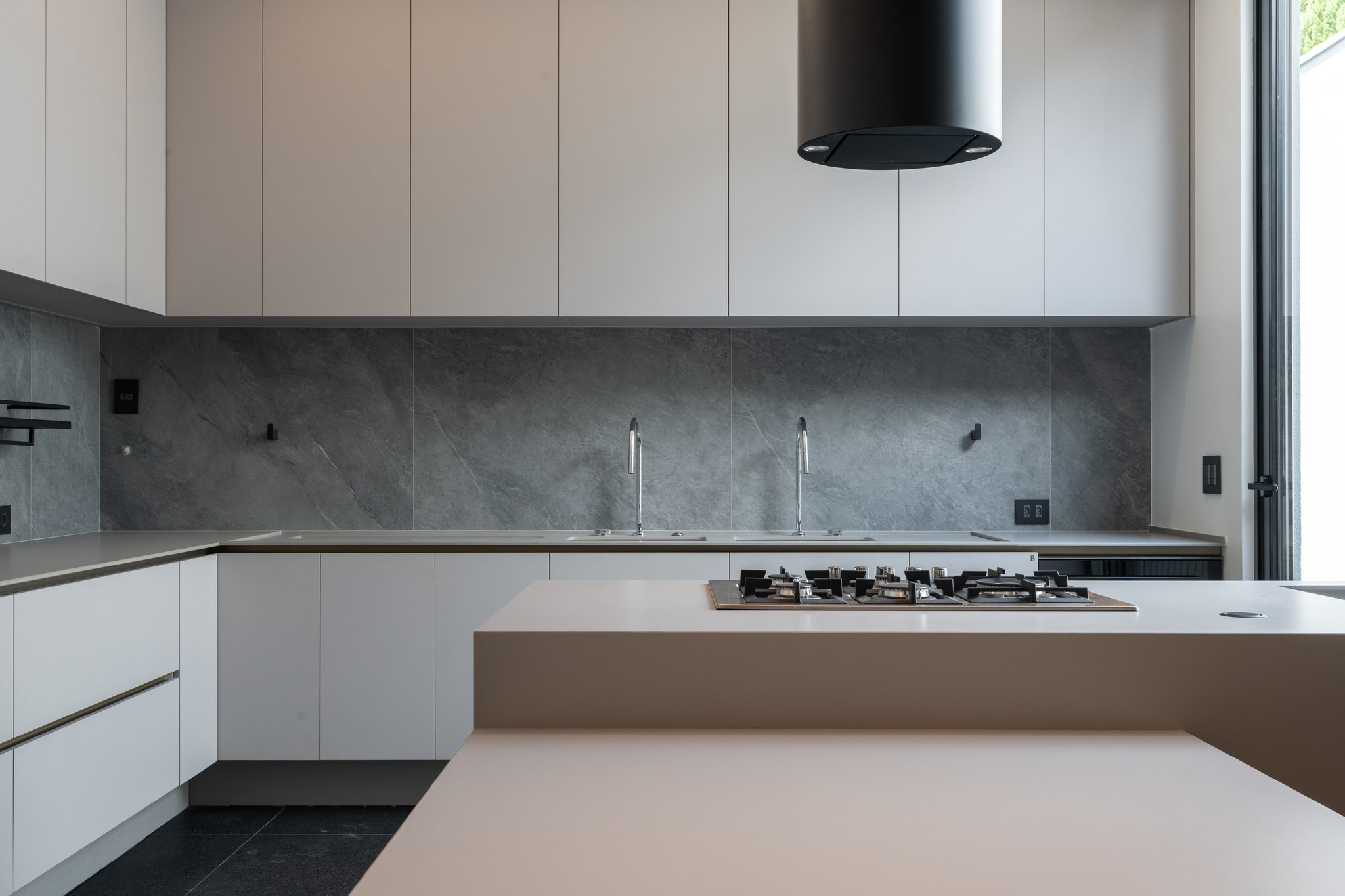 Detalhe da cozinha com revestimento em pedra cinza, cooktop a gás e bancada em duas alturas