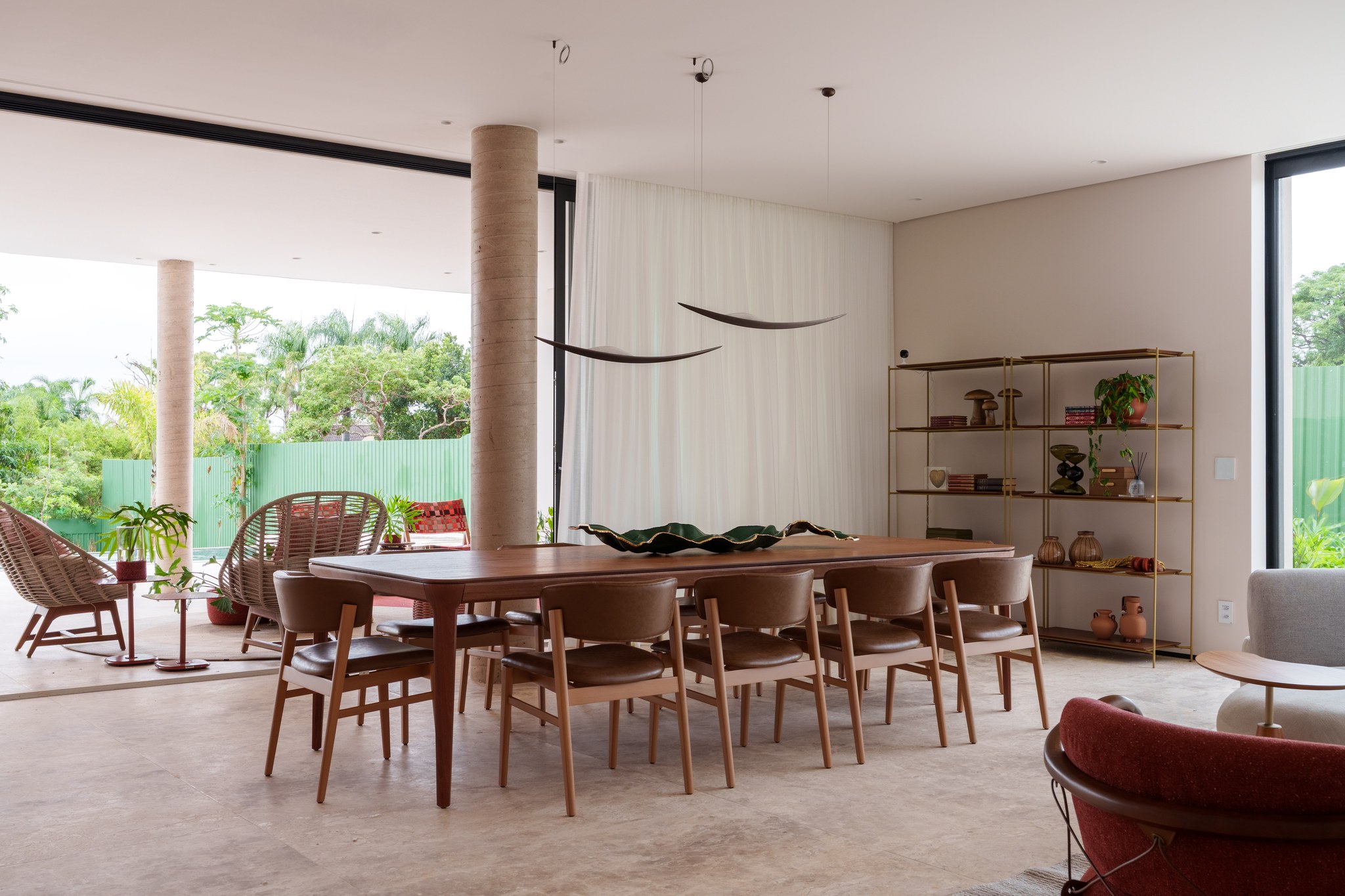 Sala integrada com mesa de jantar em madeira maciça, poltronas vermelhas e prateleiras com objetos