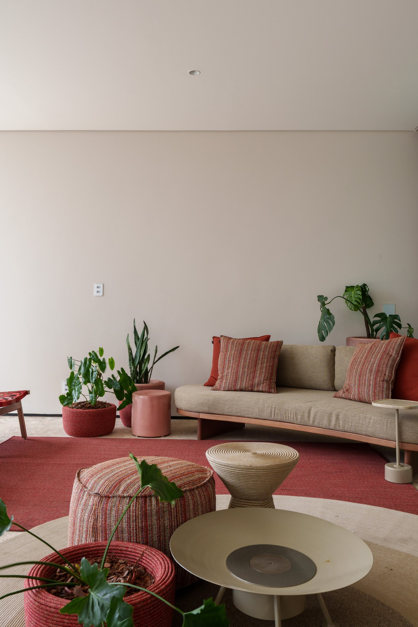 Sala de estar com sofá bege, almofadas listradas e vasos de plantas junto à parede
