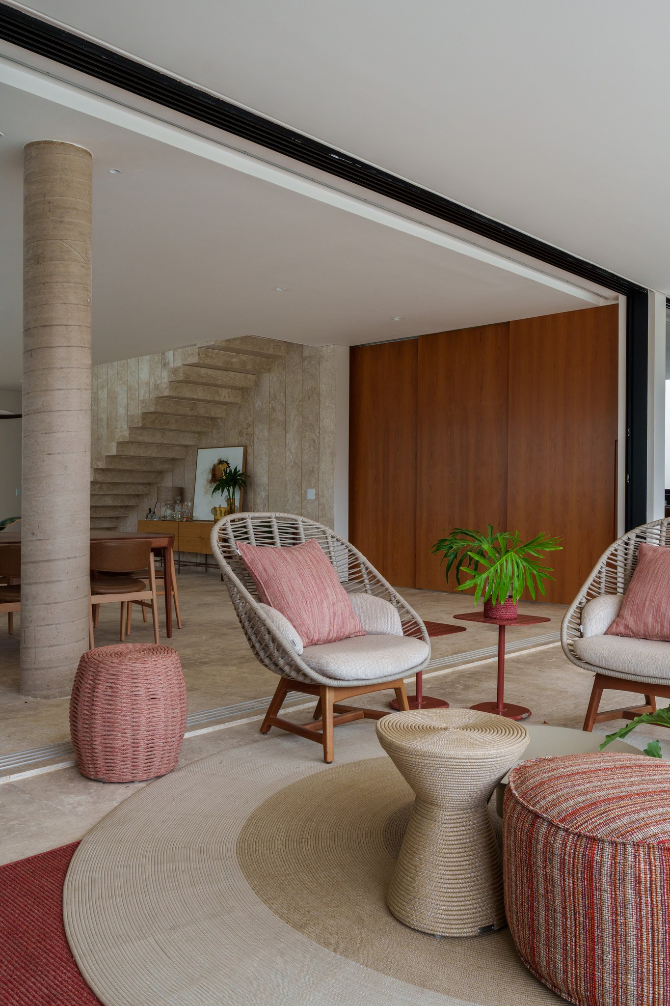Terraço coberto com poltronas trançadas, pufes e mesa lateral sobre tapete circular