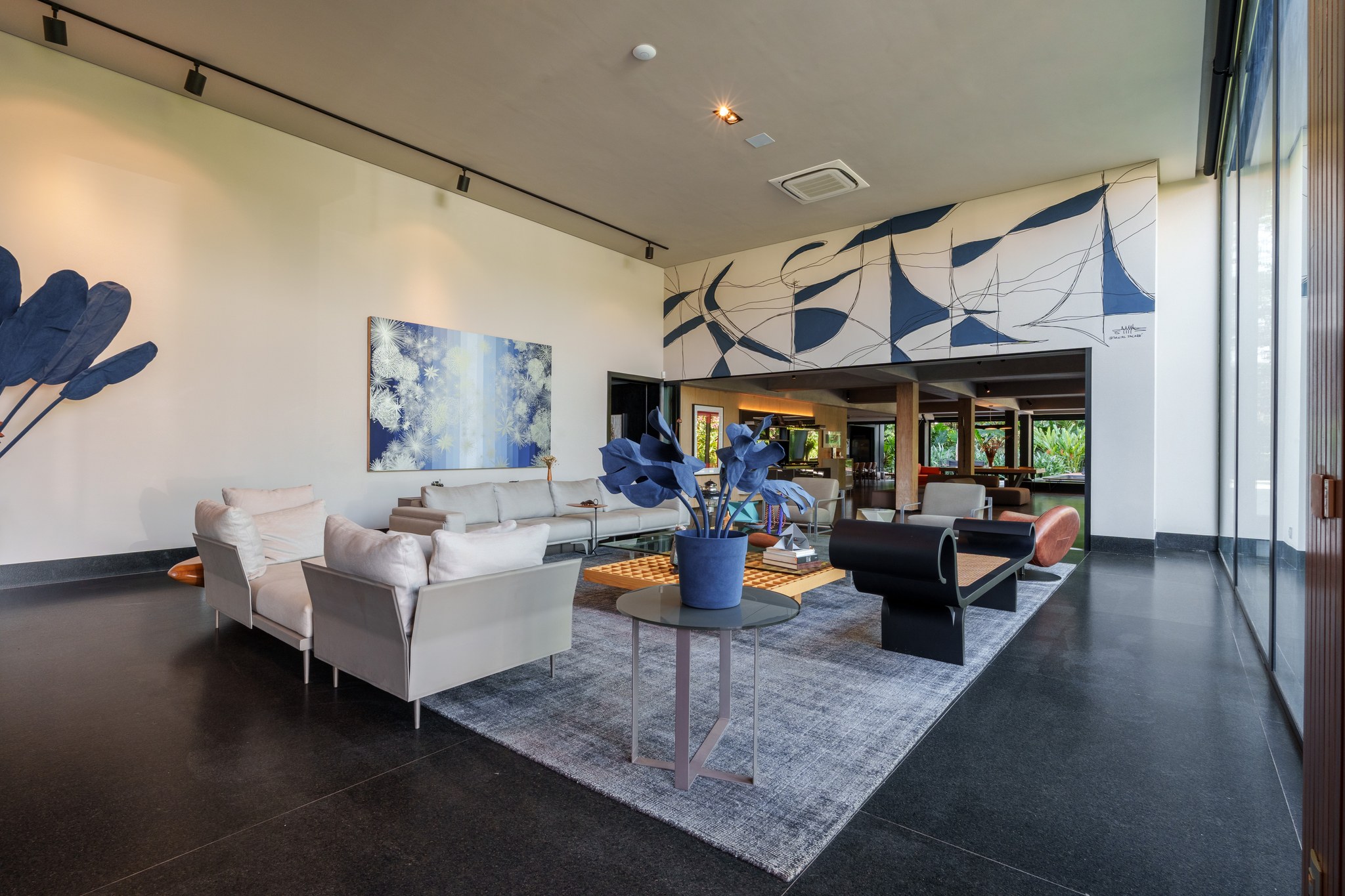 Sala de estar de pé-direito duplo, com mural artístico em azul e branco e mobiliário claro