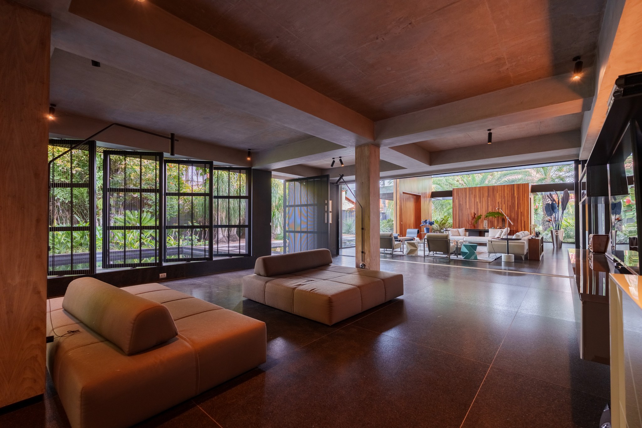 Sala de estar com pufes de couro, piso em granito polido e vista para o living principal ao fundo