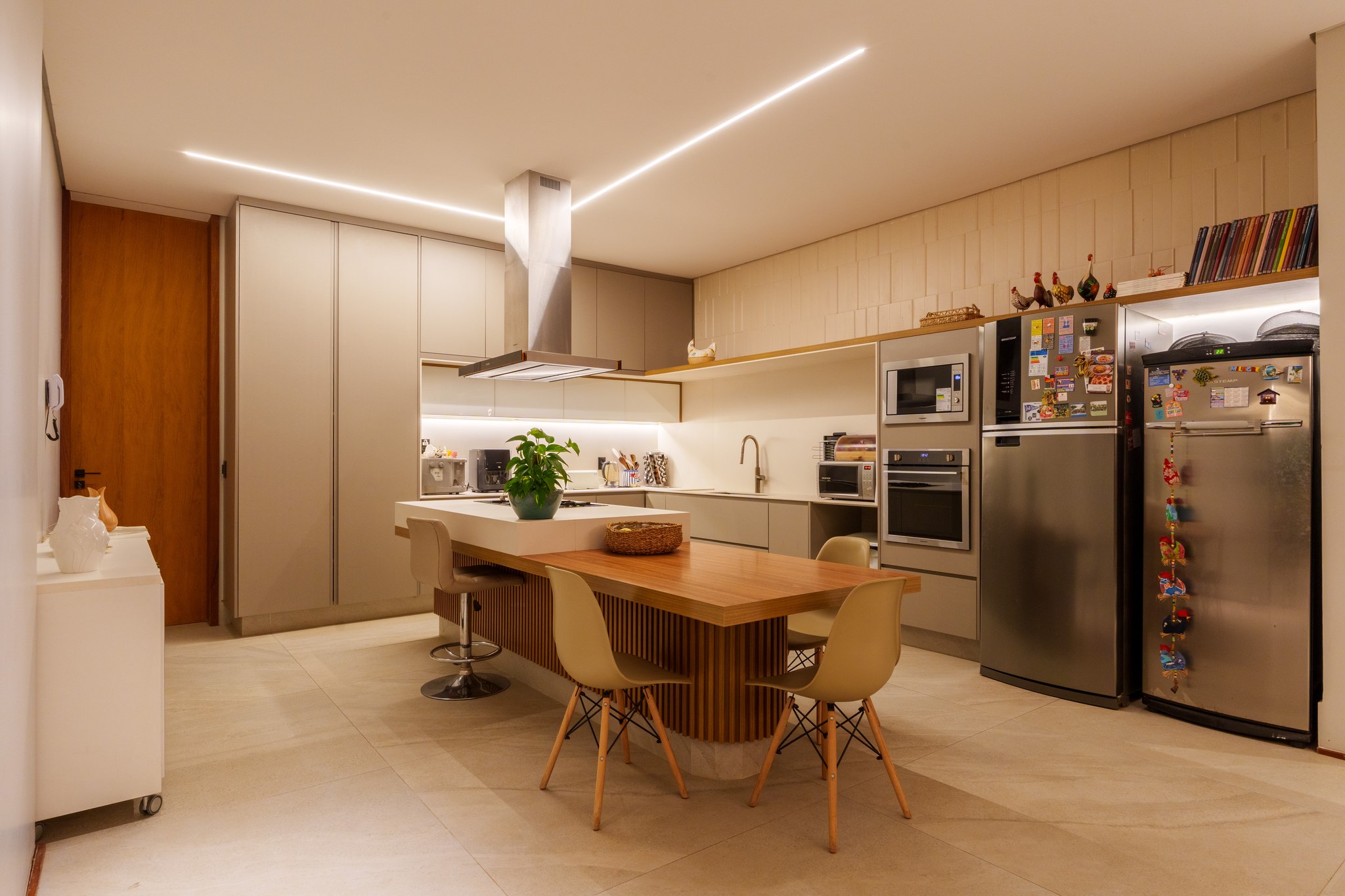 Cozinha em tons neutros com ilha central, mesa de jantar em madeira e eletrodomésticos em inox