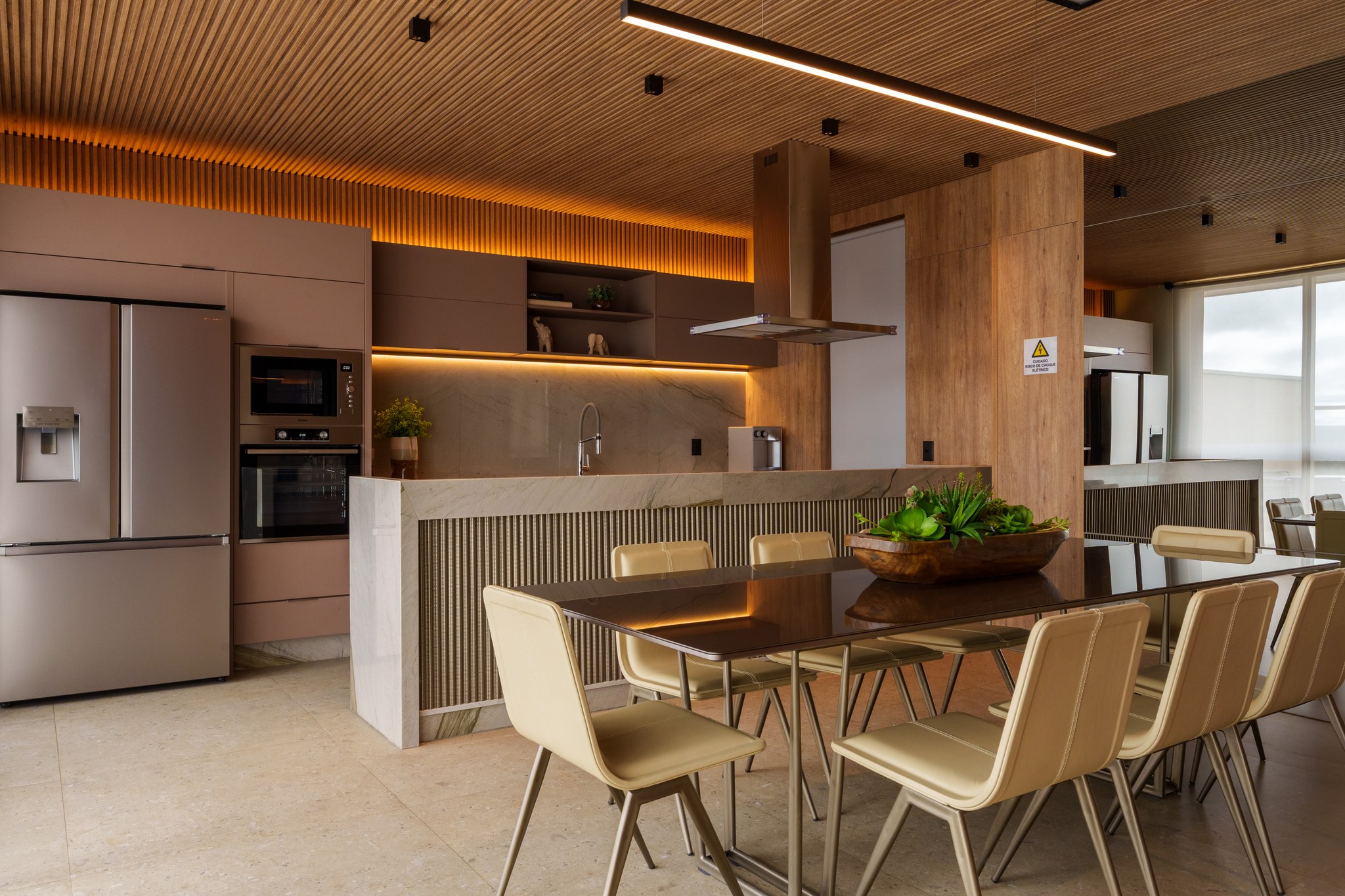 Cozinha em tons de terracota com coifa suspensa, ilha de jantar e vista para a sala do apartamento vizinho refletida