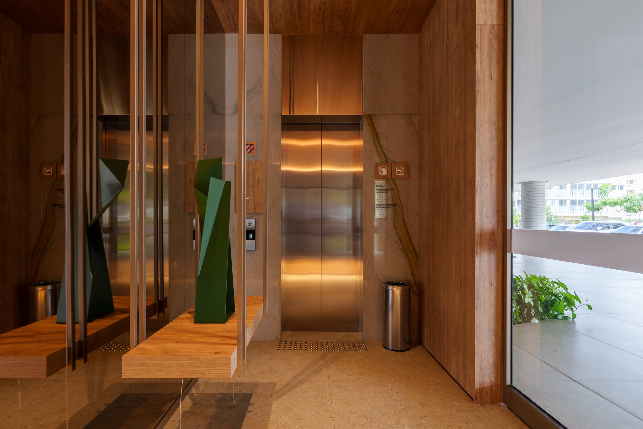 Hall dos elevadores no pavimento, com revestimento em mármore e portas em aço escovado