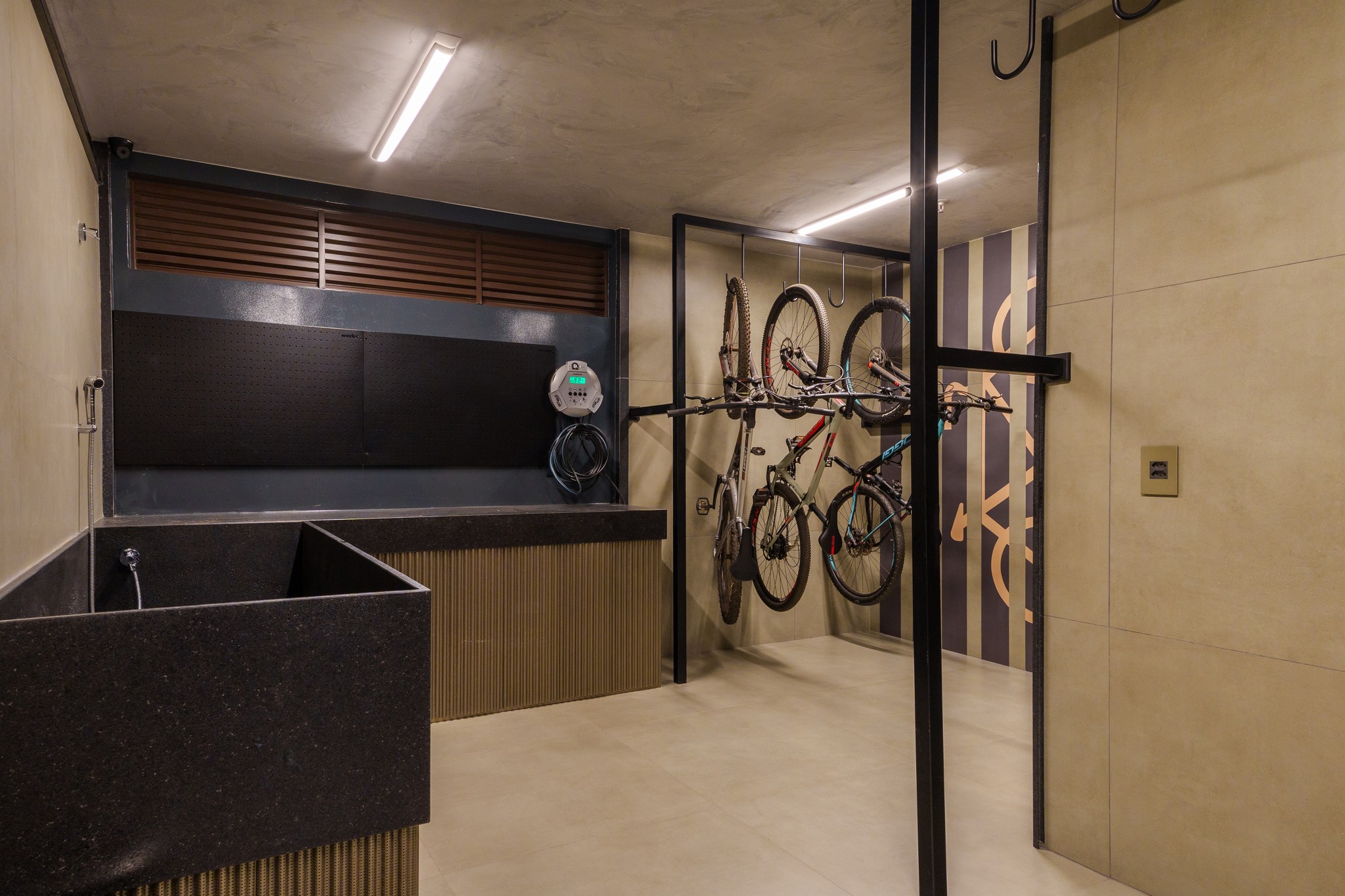Área de serviço com bancada em granito preto, suporte para bicicletas suspenso e depósito técnico