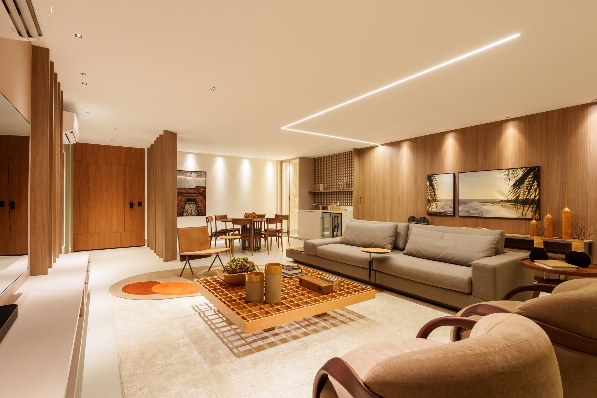 Sala de estar aberta para a sala de jantar, com quadros de praia e adega climatizada ao fundo