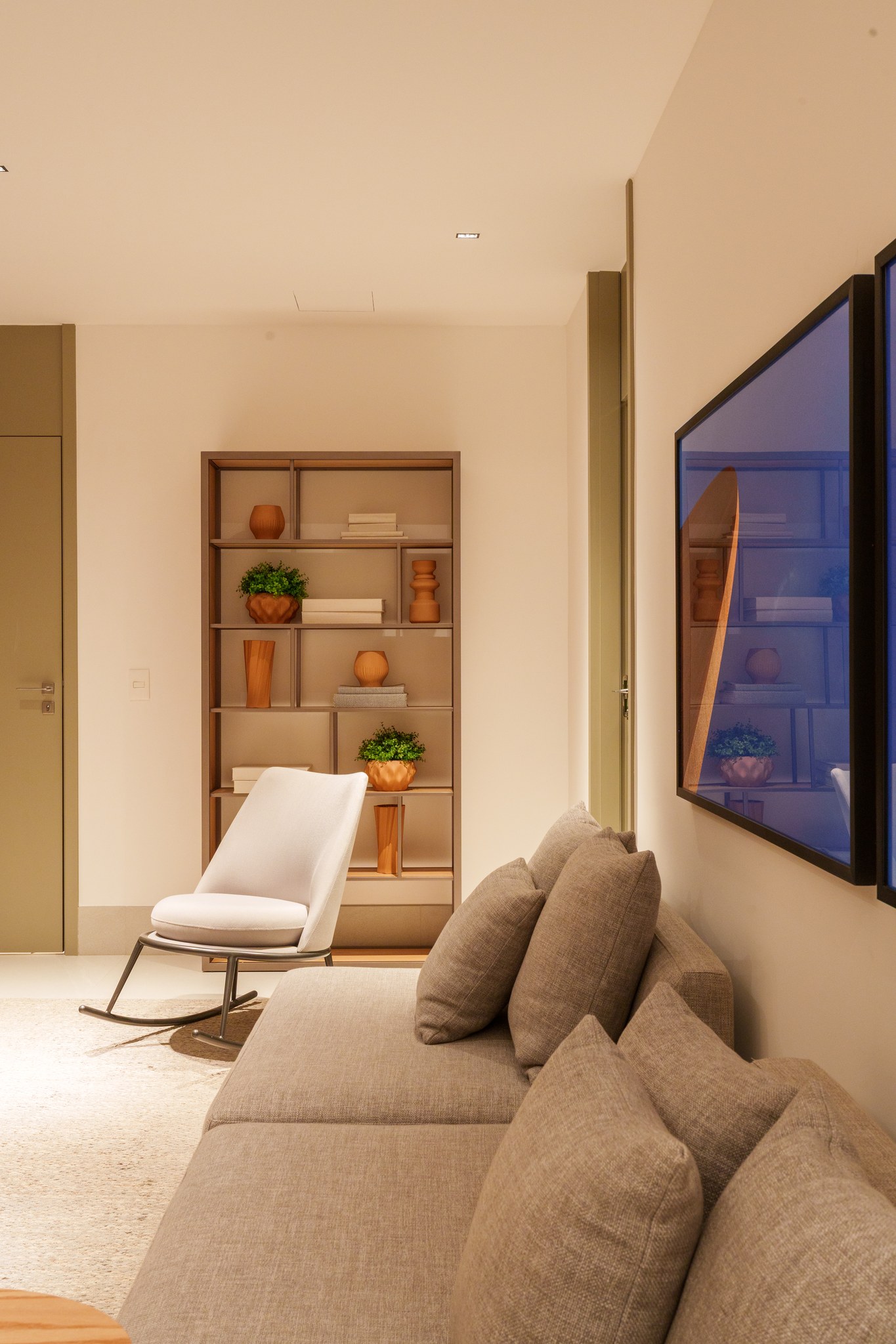 Sala de estar com estante decorativa iluminada, poltrona branca reclinável e quadros emoldurados refletidos no espelho