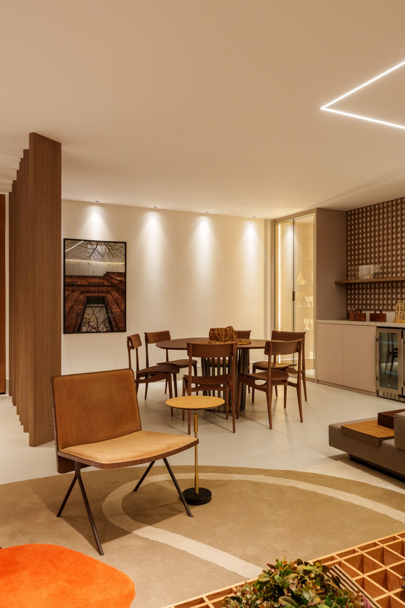 Sala de jantar com mesa oval, cadeiras de madeira e adega climatizada junto ao bar em treliça