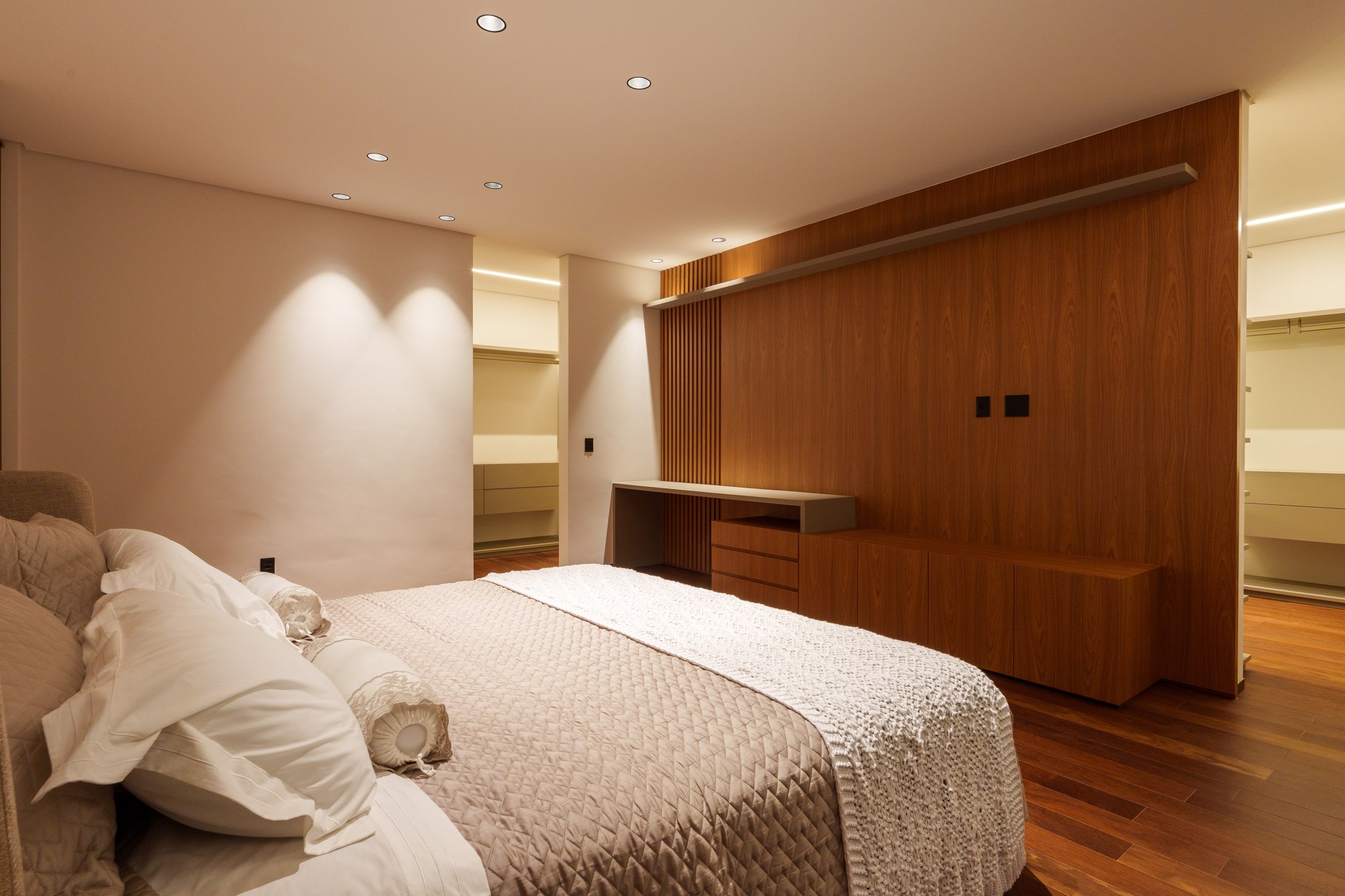 Closet planejado em madeira com iluminação embutida, ripas verticais e bancada de apoio