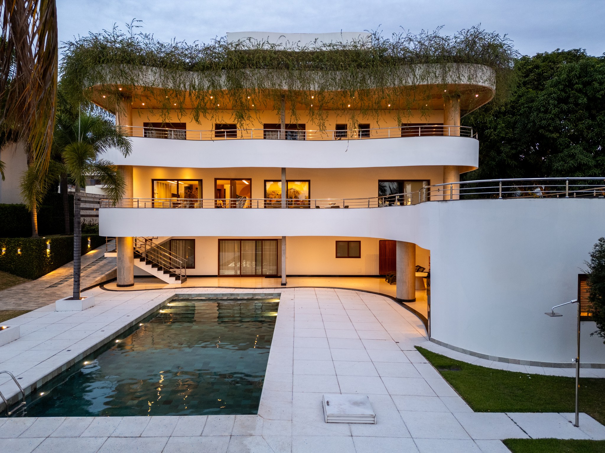 Fachada dos fundos da residência modernista, com varandas curvas sobrepostas e piscina ao entardecer