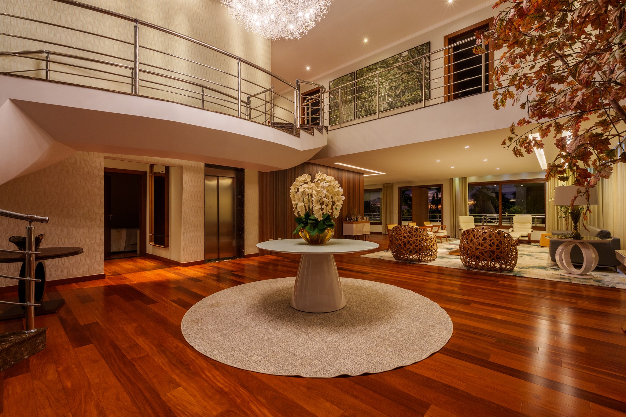 Hall de entrada de pé-direito duplo, com elevador, mesa redonda central e sala de estar ao fundo