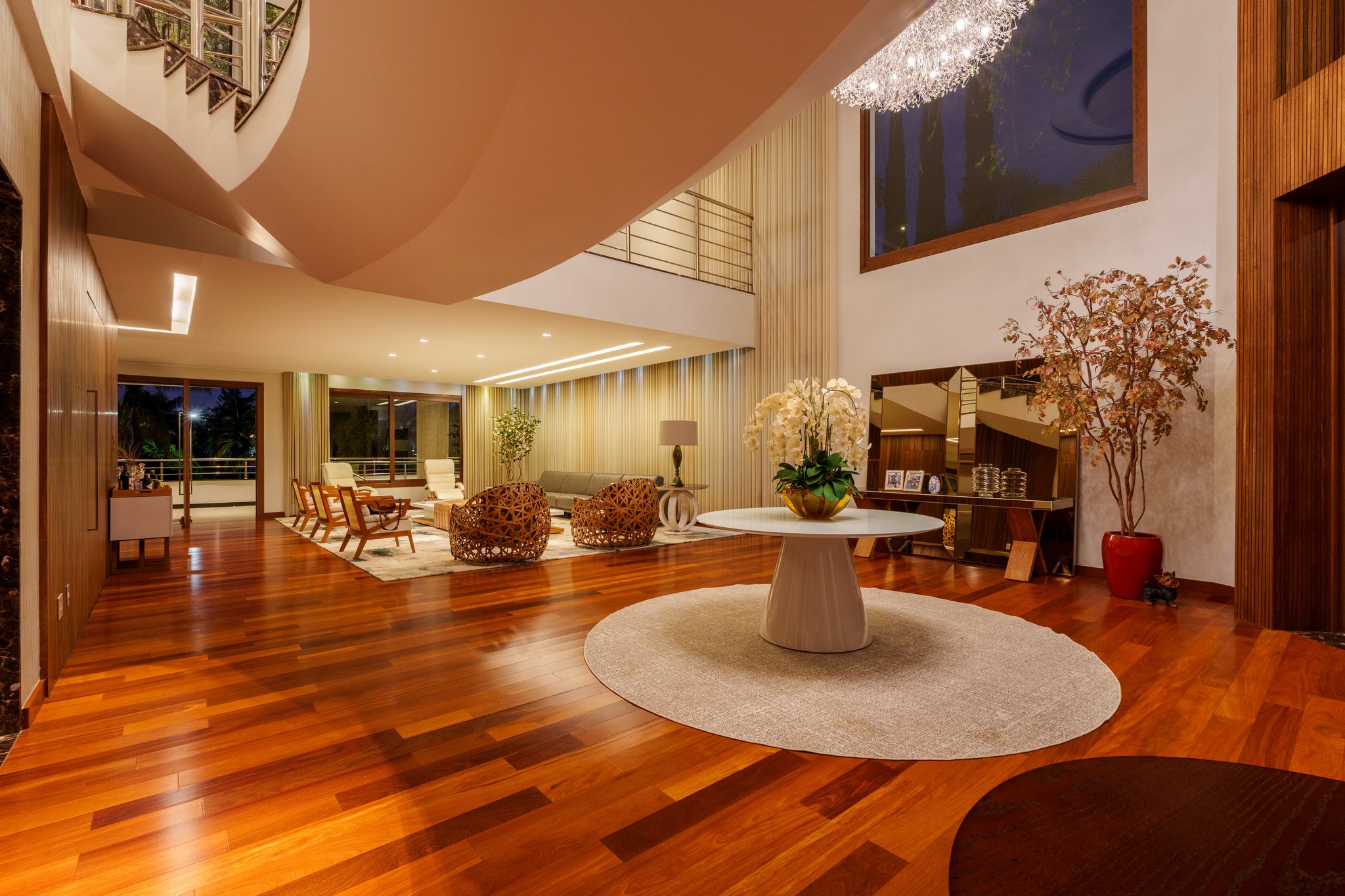 Sala de estar ampla com poltronas trançadas, tapete estampado e varanda curva com vista para o jardim