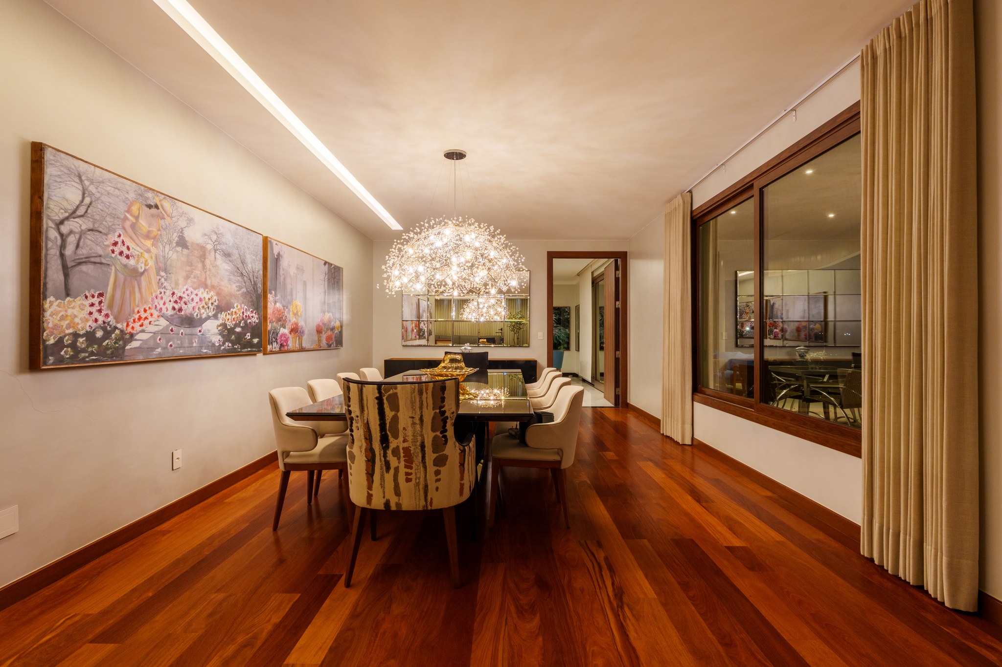 Sala de jantar com quadros florais, lustre orgânico suspenso e mesa espelhada para oito lugares