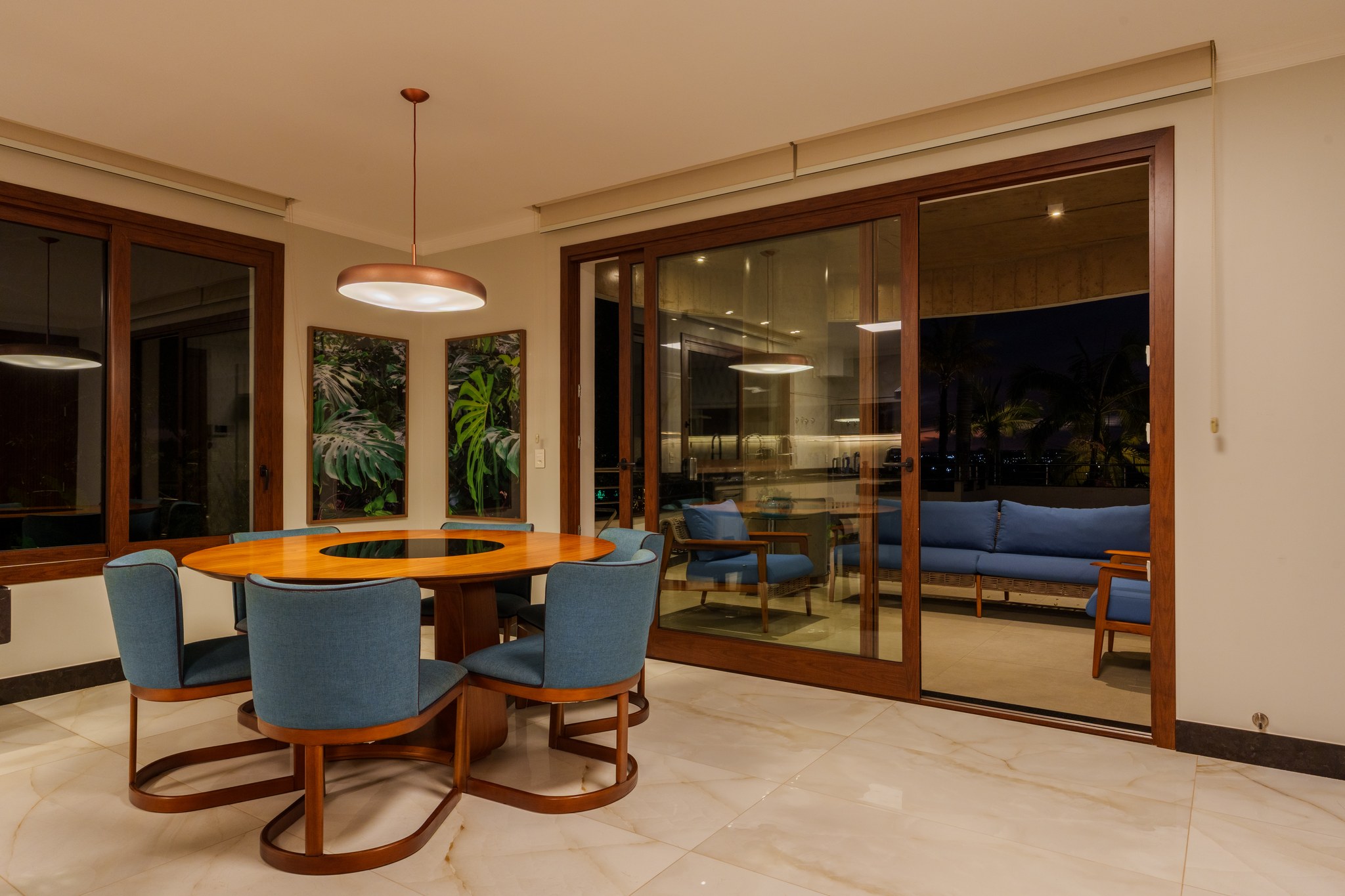 Sala de jantar redonda com cadeiras azuis, mesa de madeira maciça e vista para a sala de estar
