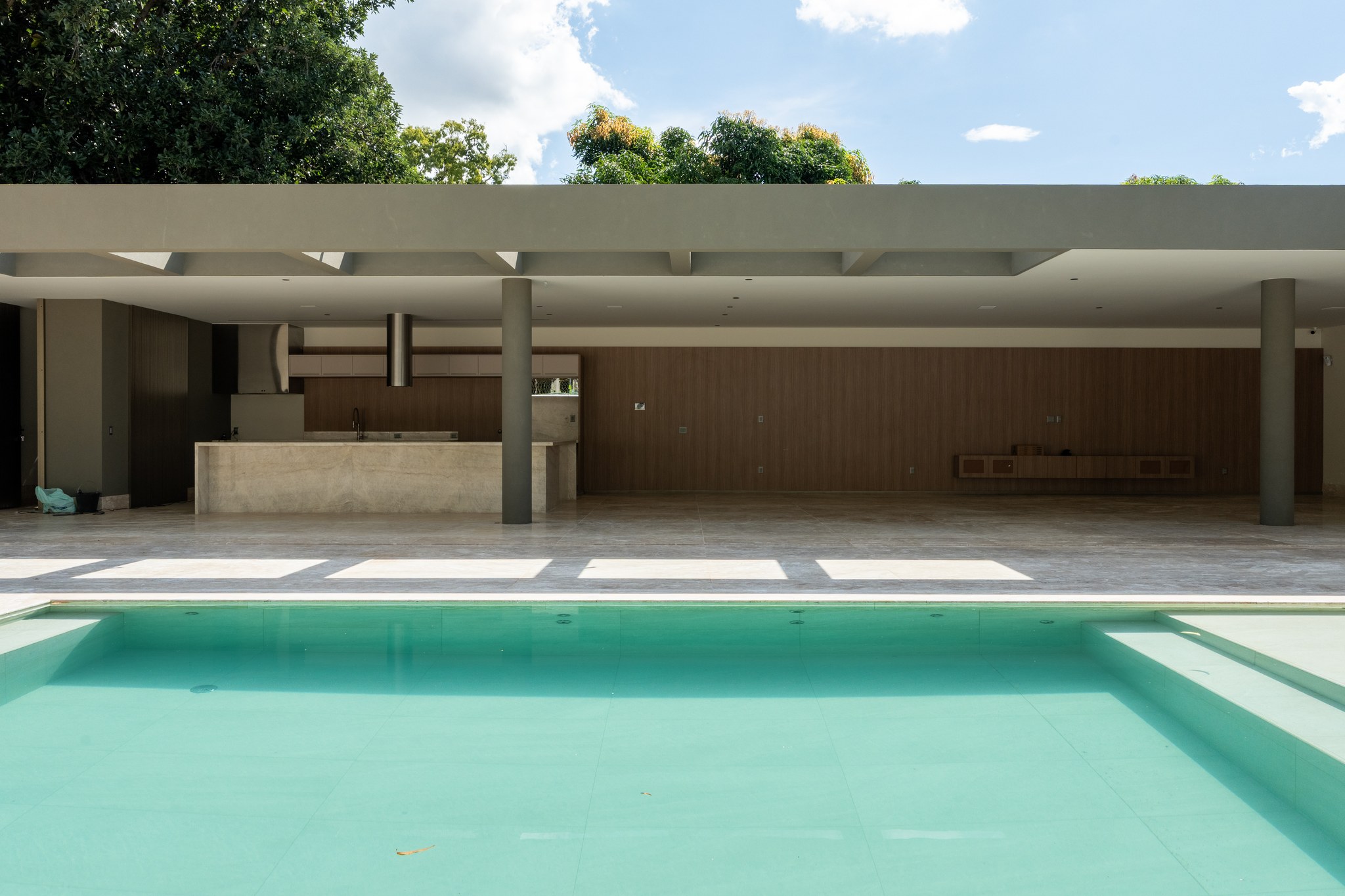 Vista da piscina e da área de estar coberta, ainda em fase de acabamento, com bancada em travertino