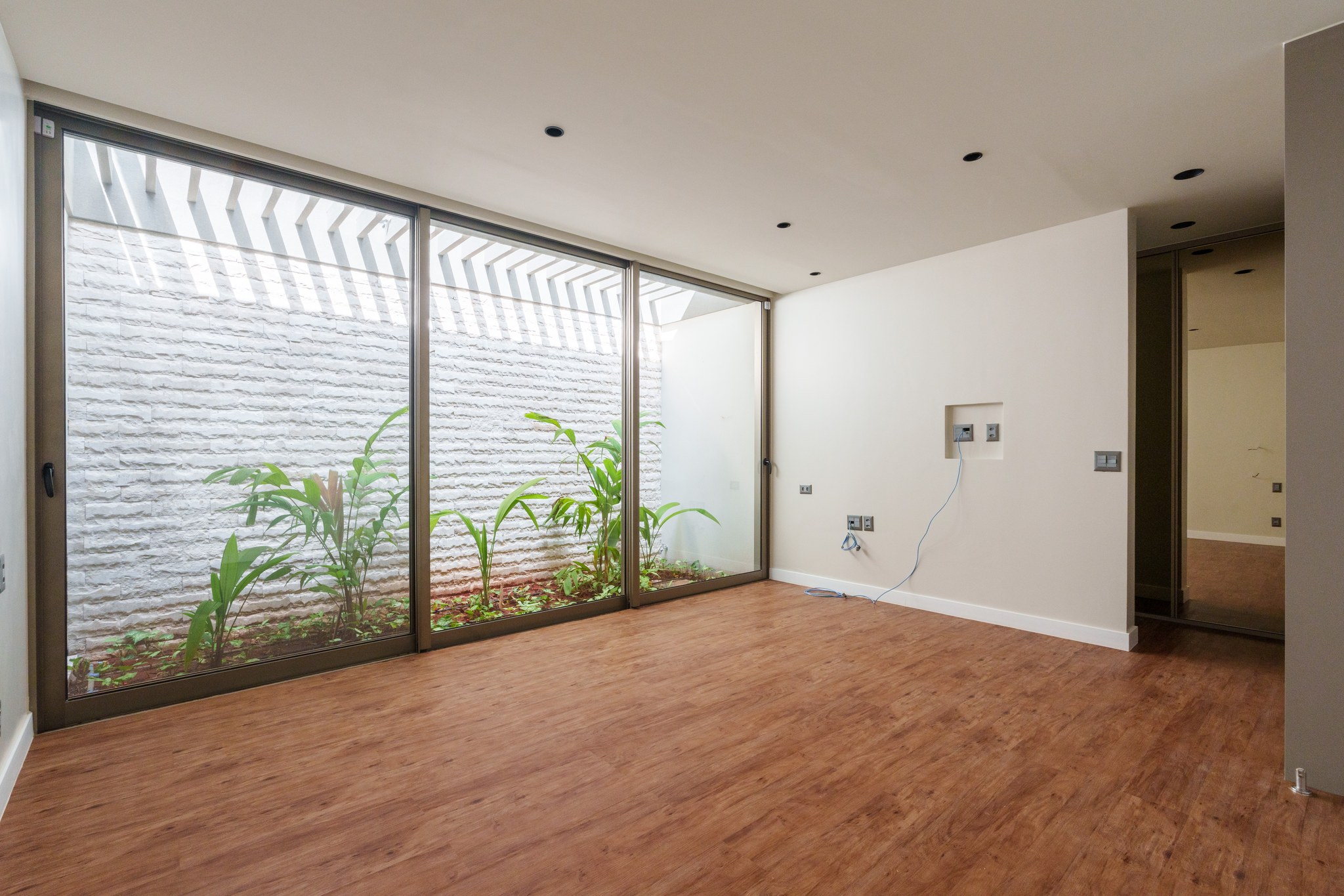 Quarto vazio em acabamento, com piso vinílico amadeirado e portas de vidro para o jardim interno