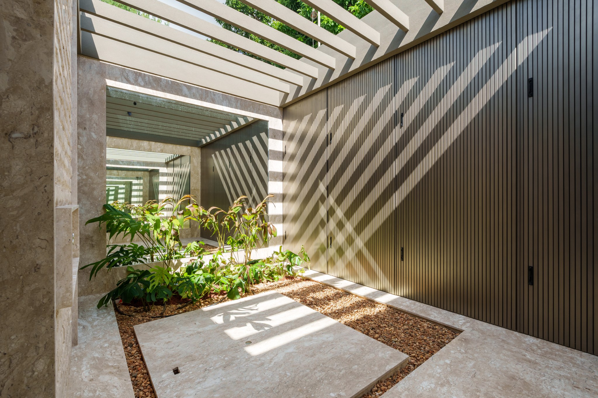 Pátio interno com jardineira de plantas tropicais, jardim de inverno e portão ripado em metal