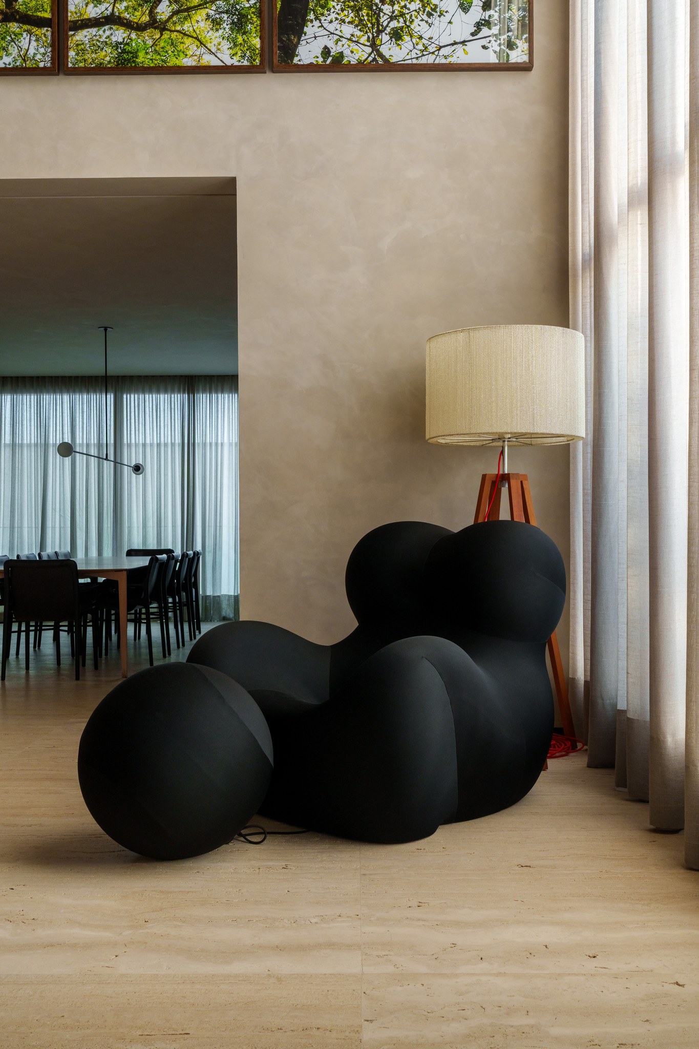 Poltrona escultural preta e luminária de piso de canto, diante de galeria de fotografias