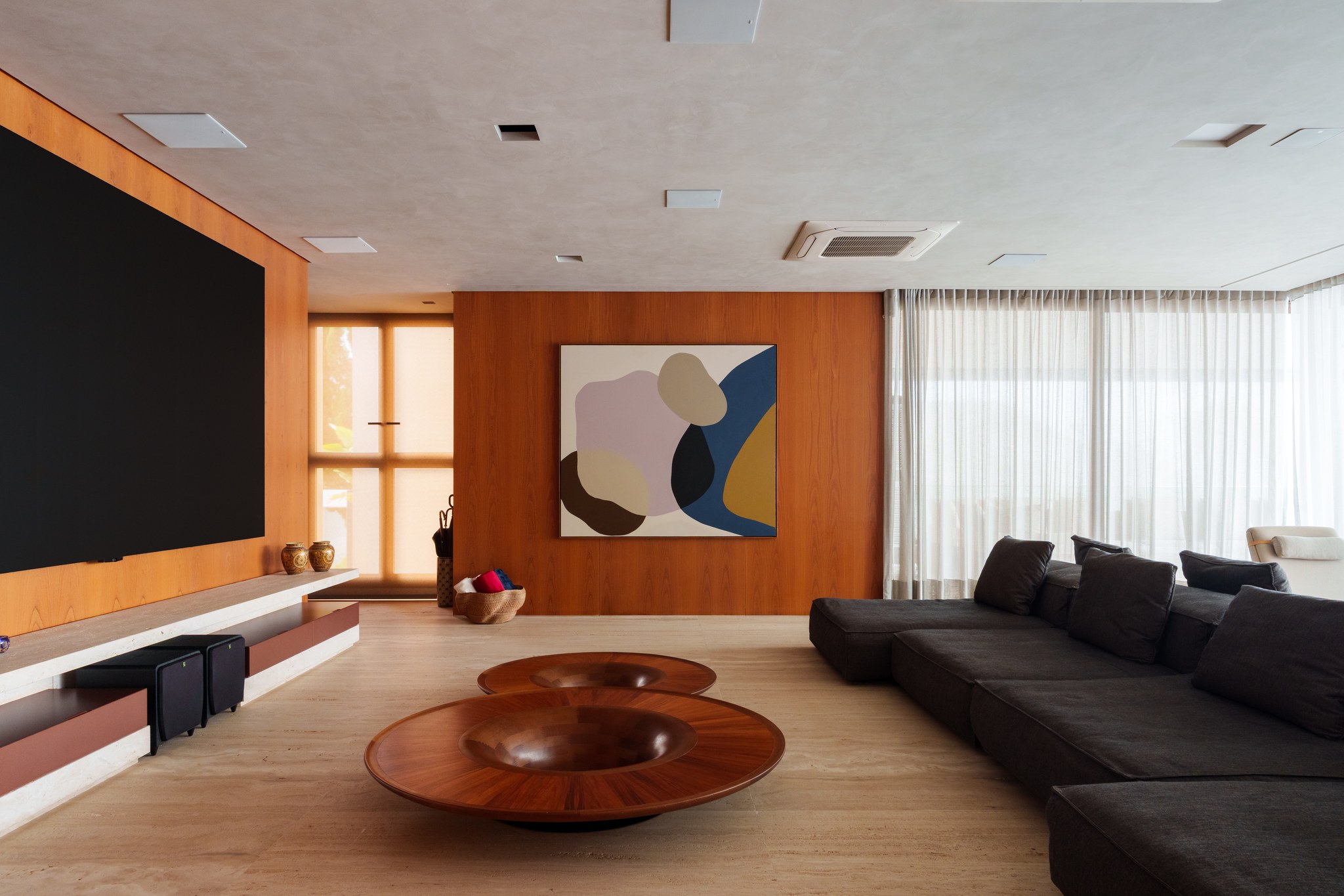Sala de home theater com painel de madeira, quadro abstrato colorido e sofá modular escuro